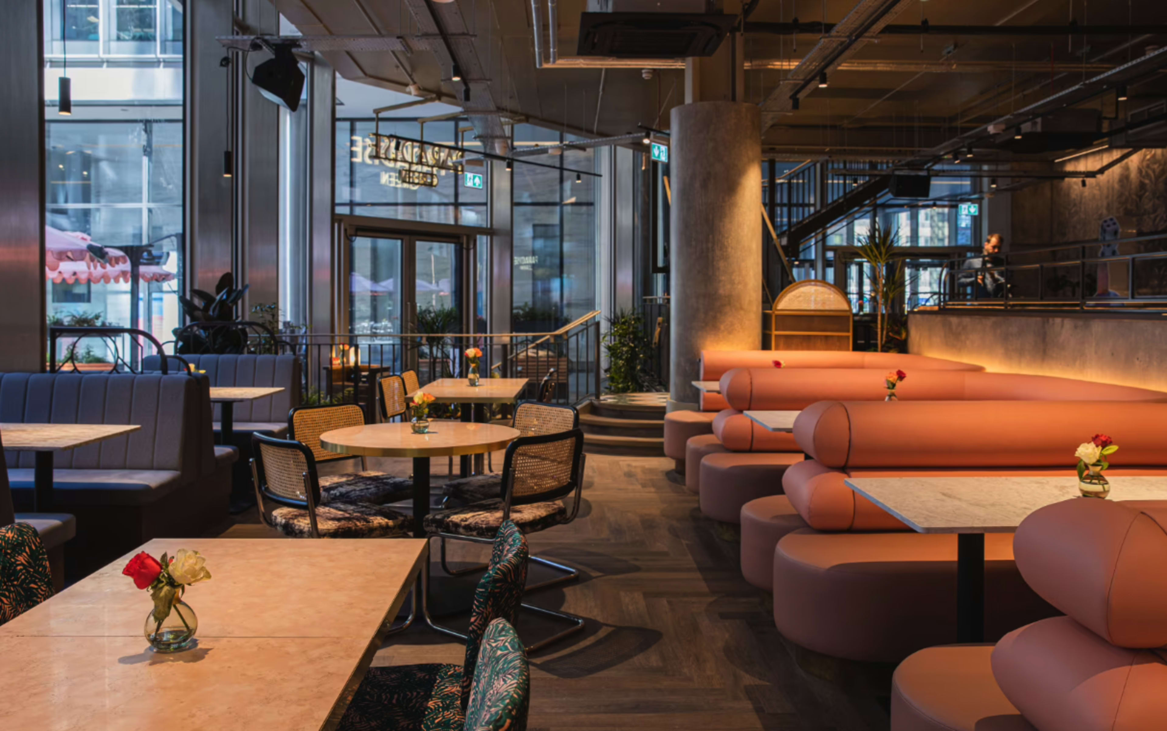 The image shows a modern restaurant interior featuring circular booths, tables, and a mix of seating arrangements, with large windows allowing natural light.