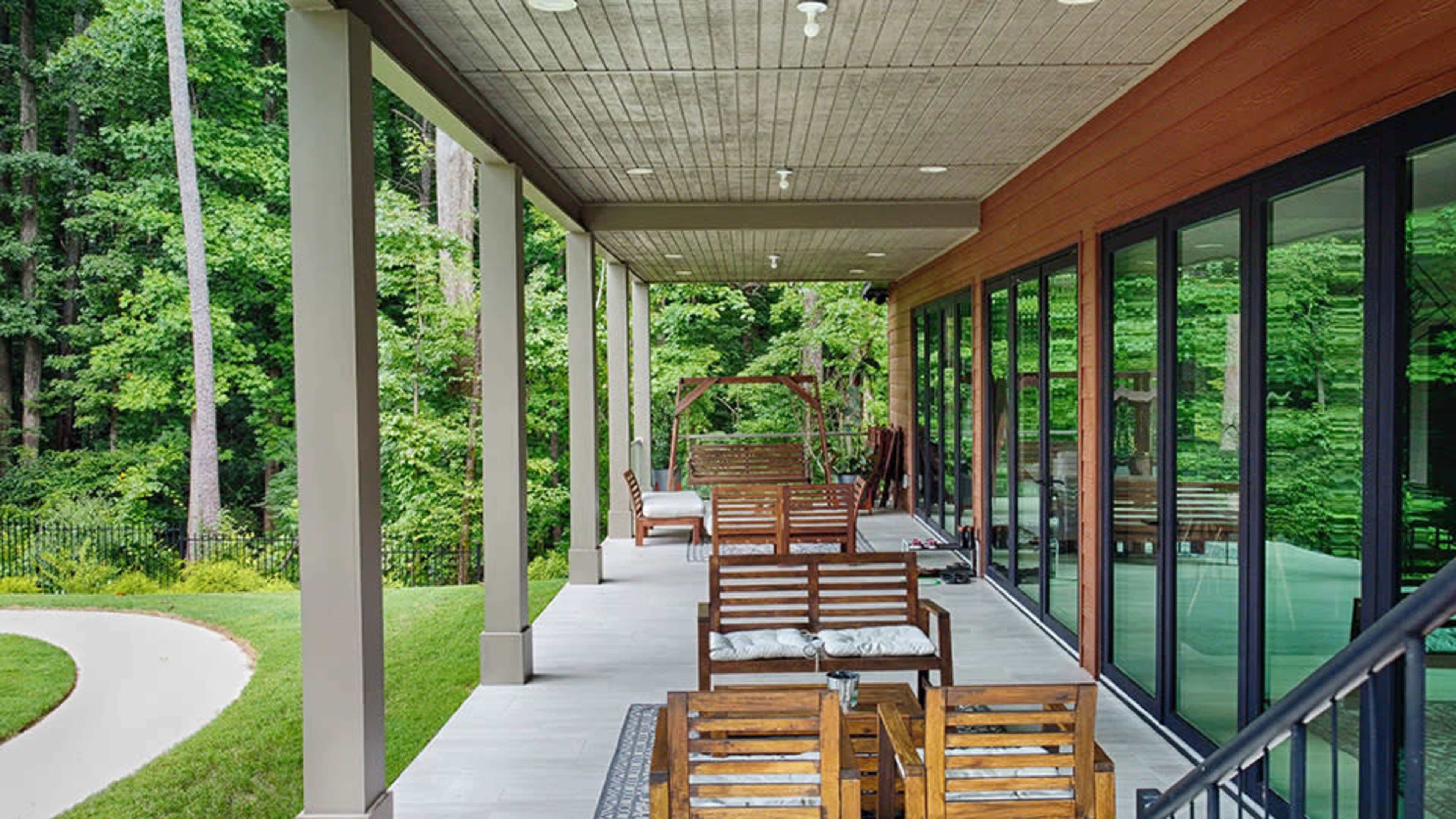 A spacious outdoor patio features wooden seating arranged along a covered area, surrounded by greenery.
