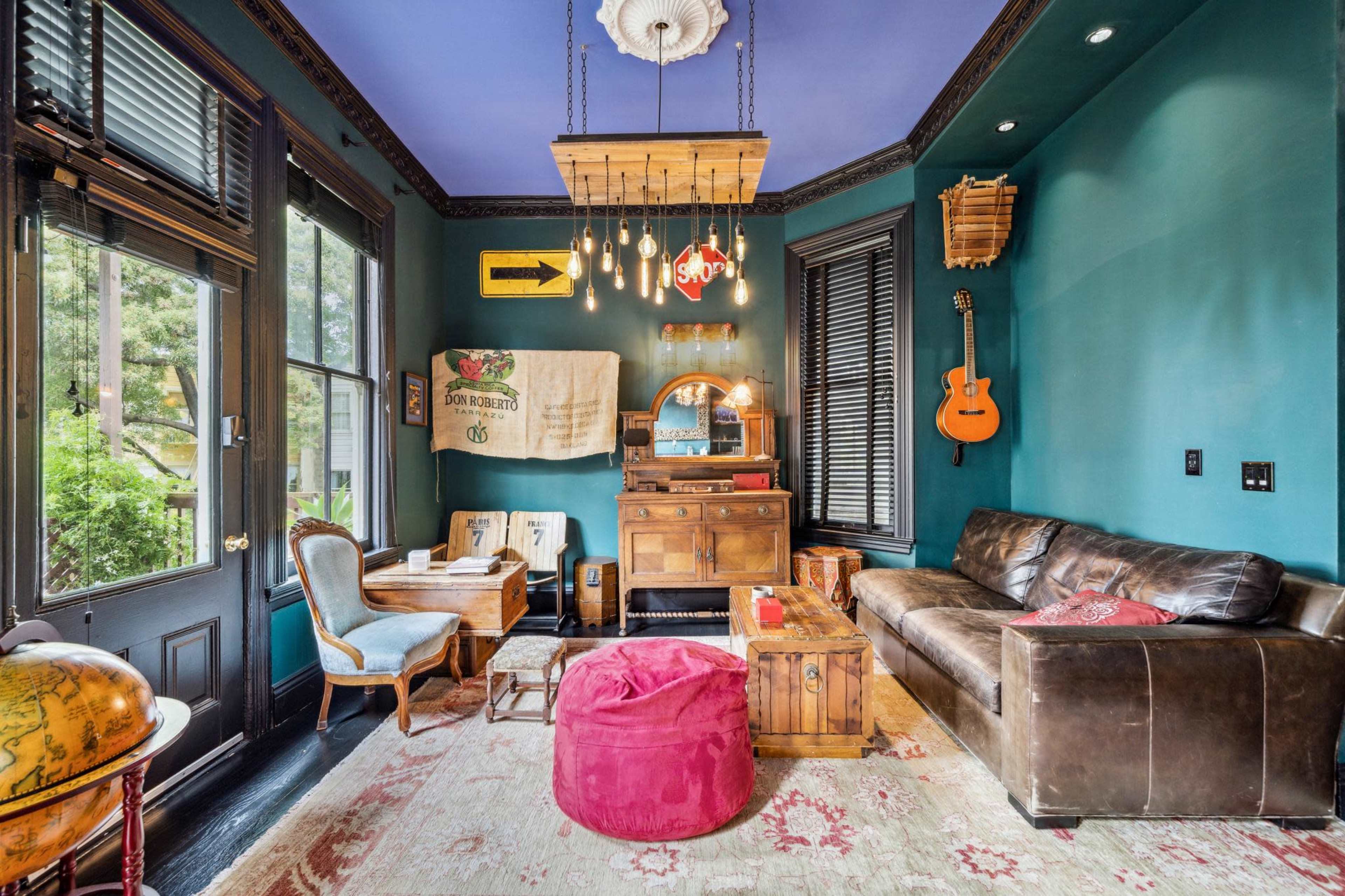 The room features a mix of vintage furniture, including a leather sofa, a wooden table, and a bright blue ceiling with pendant lights.