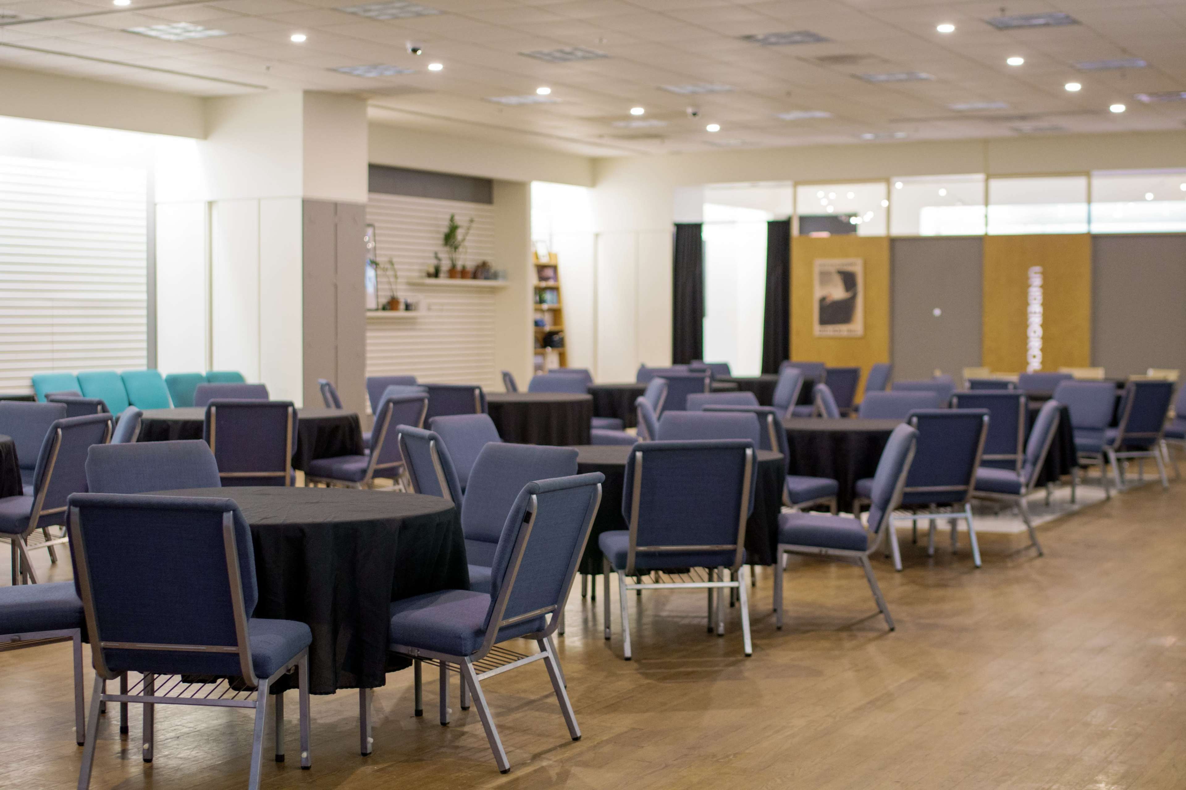 The photo shows a spacious room with rows of round tables covered in black cloth and surrounded by blue chairs.
