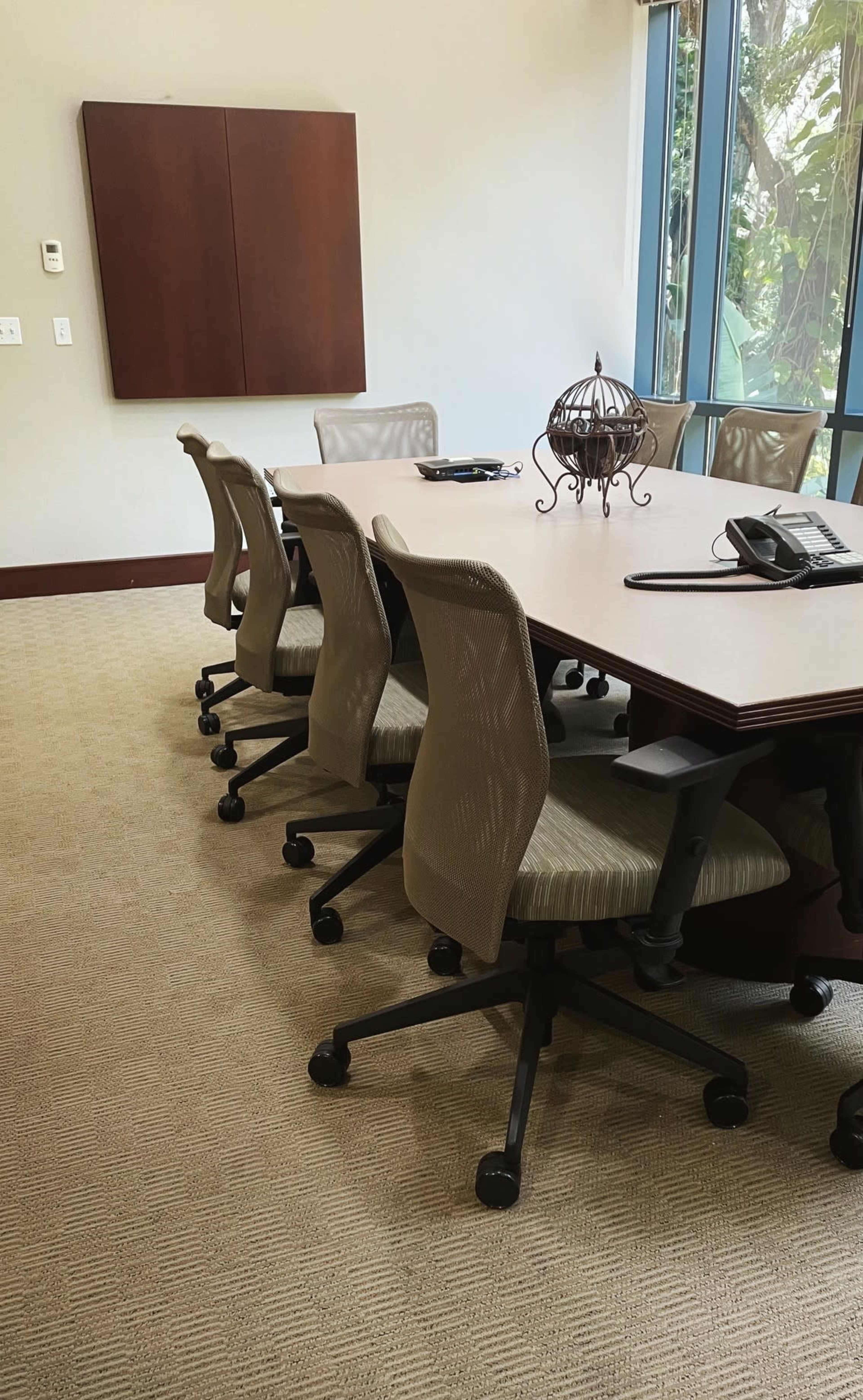 A conference room with a large table surrounded by several office chairs and a phone at one end.
