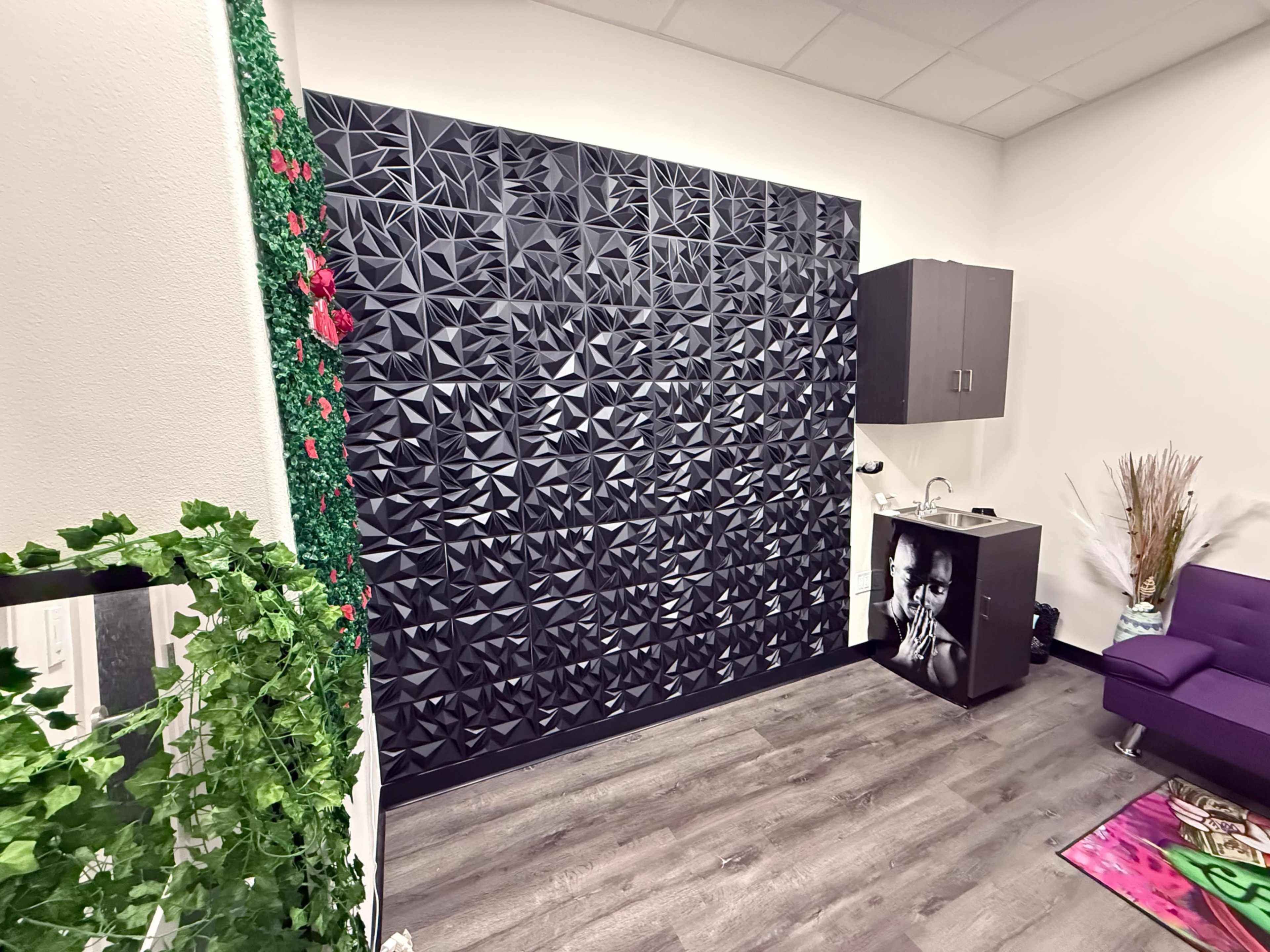 The image shows a modern room featuring a textured black wall, a small kitchenette in one corner, and a purple sofa.