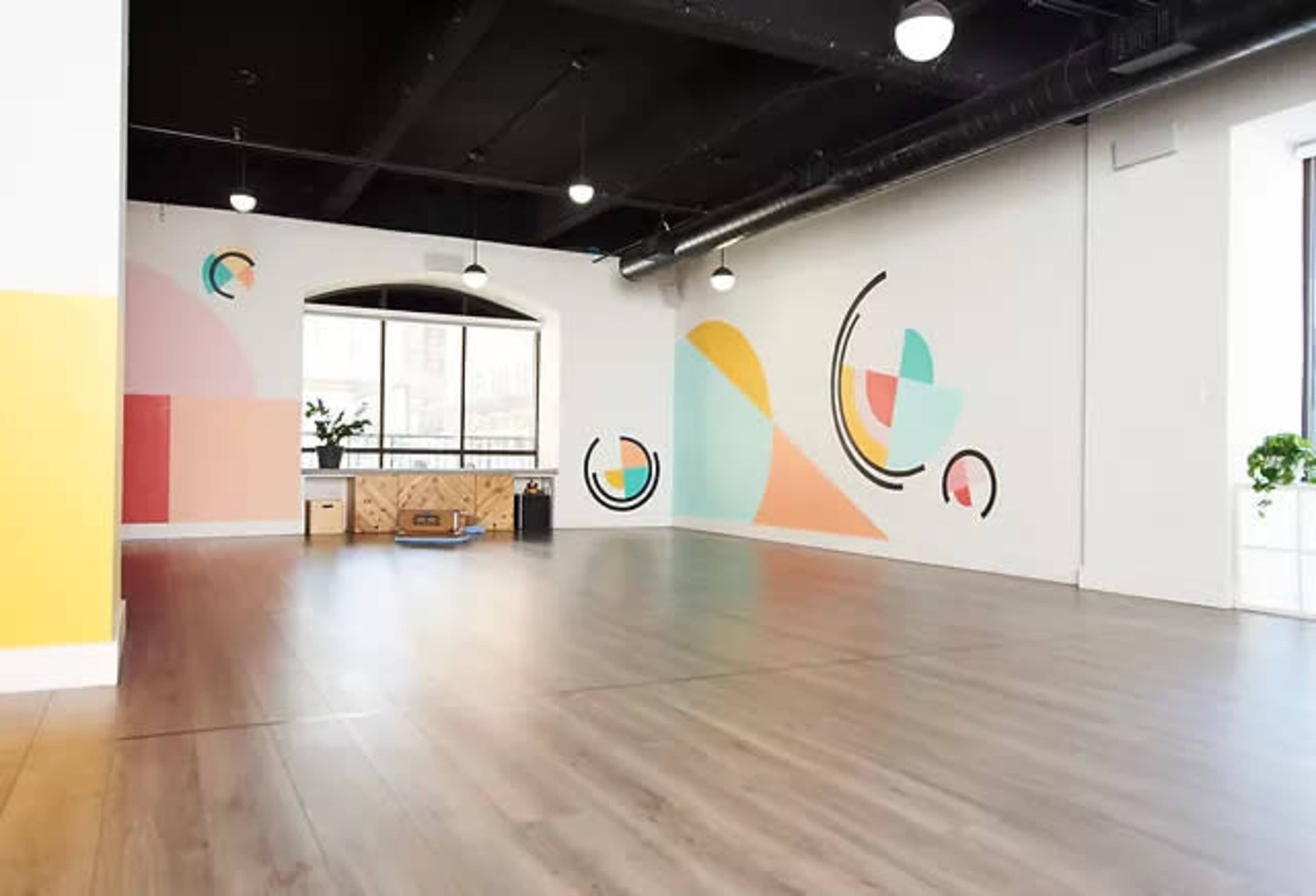 An empty room with wooden flooring and a decorative wall featuring colorful abstract shapes.