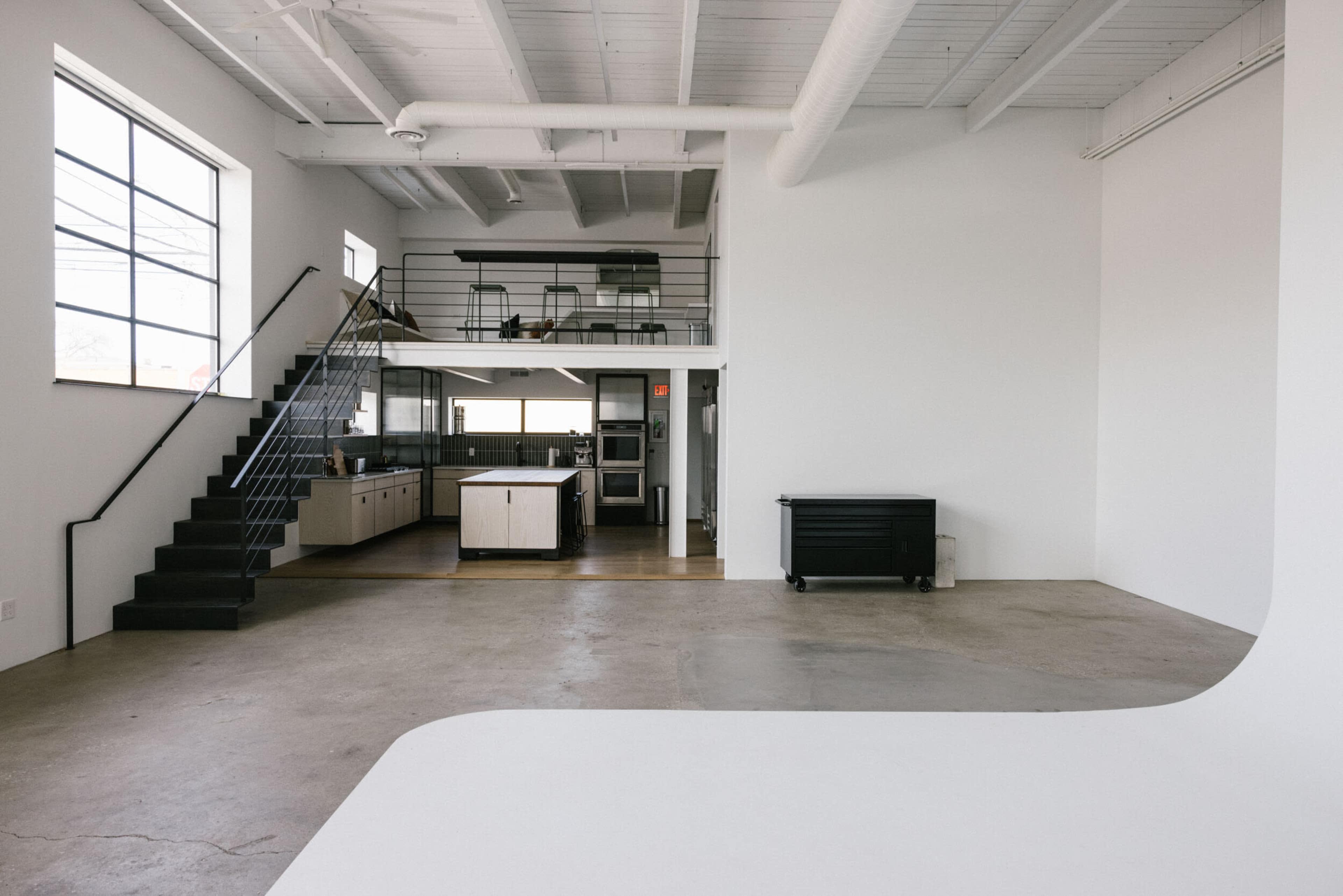 An open, minimalist space featuring a kitchen, staircase, and an area with a large, curved white surface.