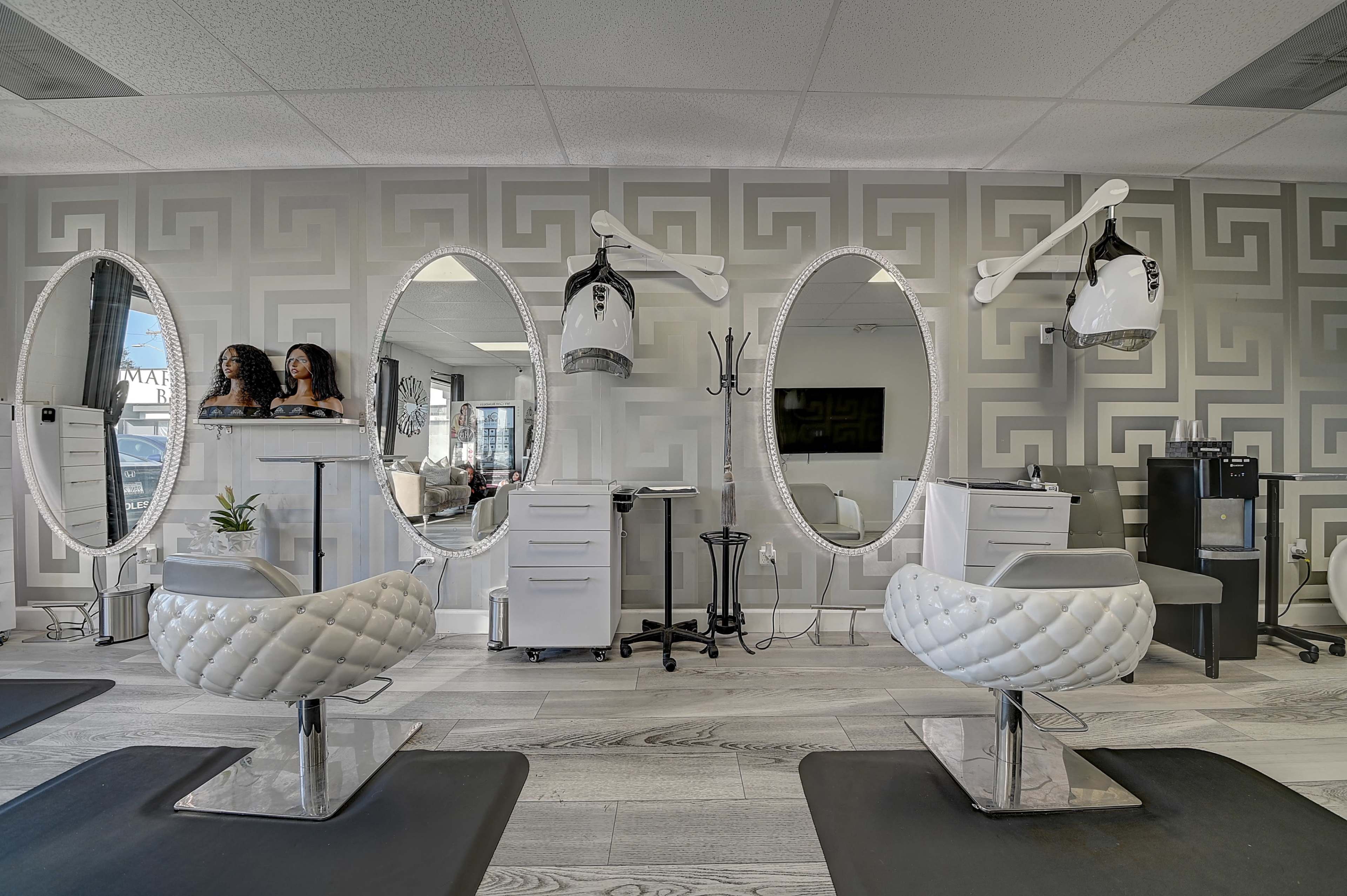 A modern salon interior with two hair styling stations, each featuring a large oval mirror and a mannequin head displayed on elevated stands.