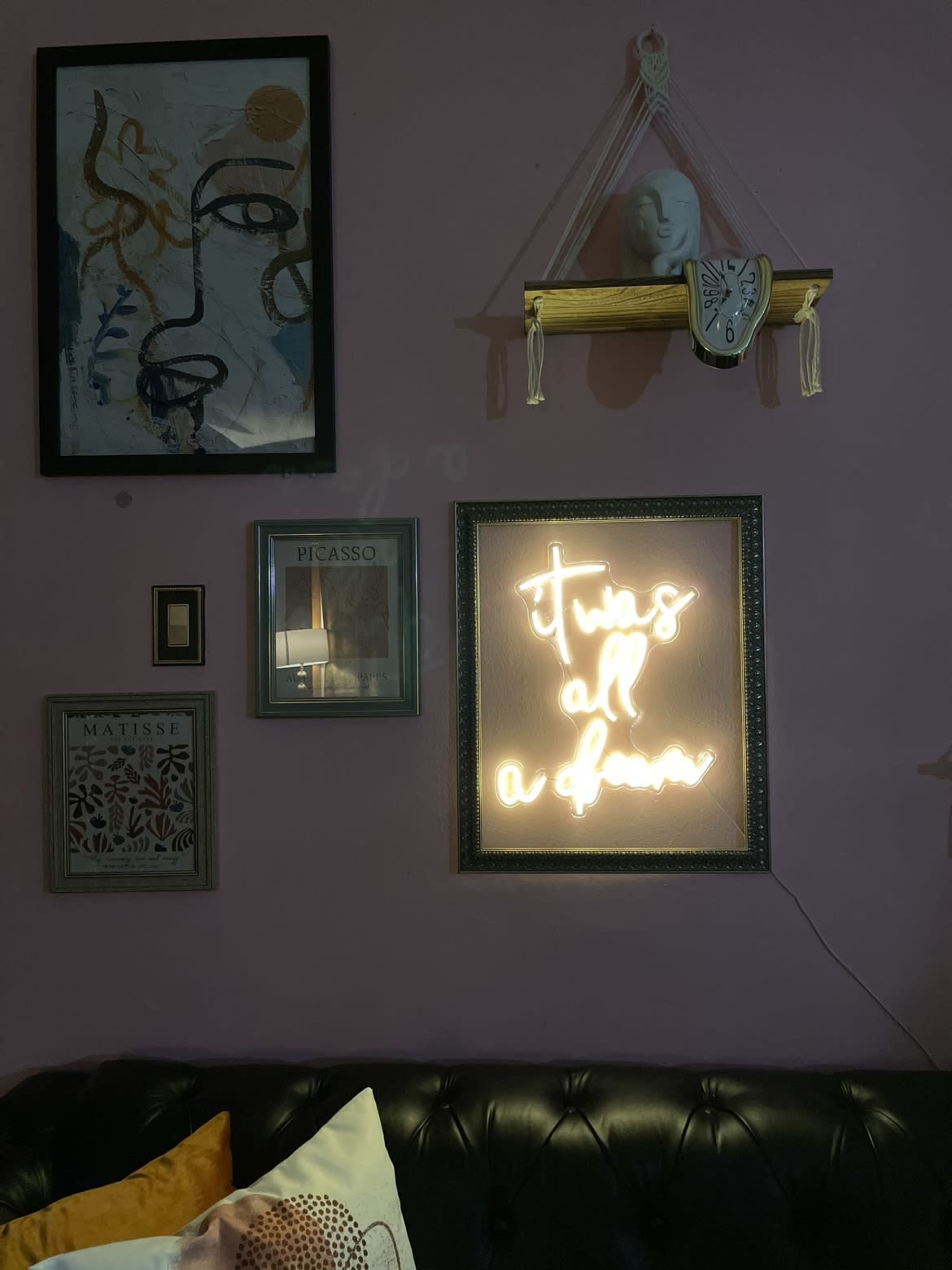 A wall adorned with various framed artworks and a neon sign that reads "It's all a dream," above a dark leather sofa.