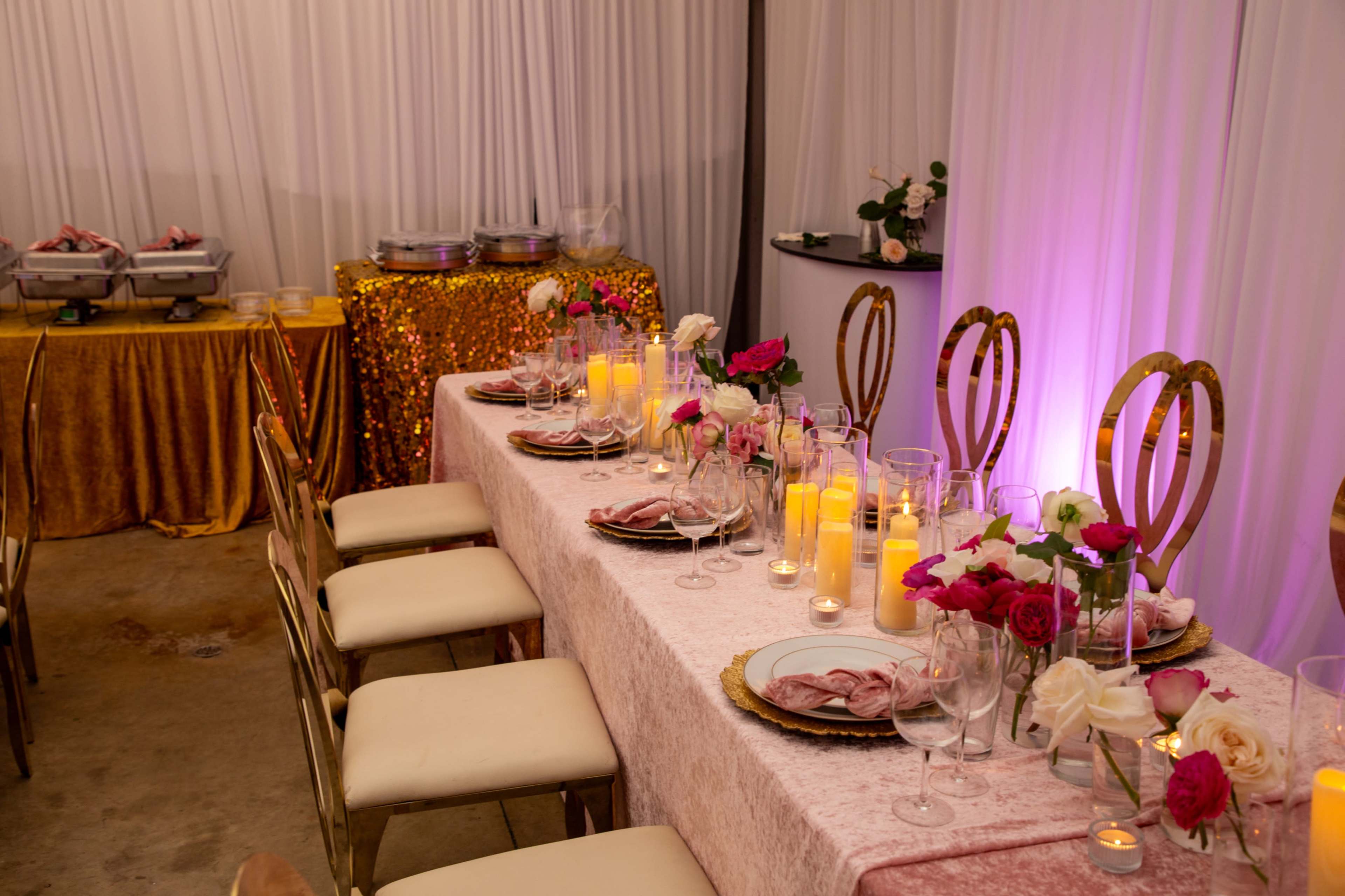A long, elegantly set table adorned with candles, flowers, and folded napkins, complemented by a golden tablecloth in the background.