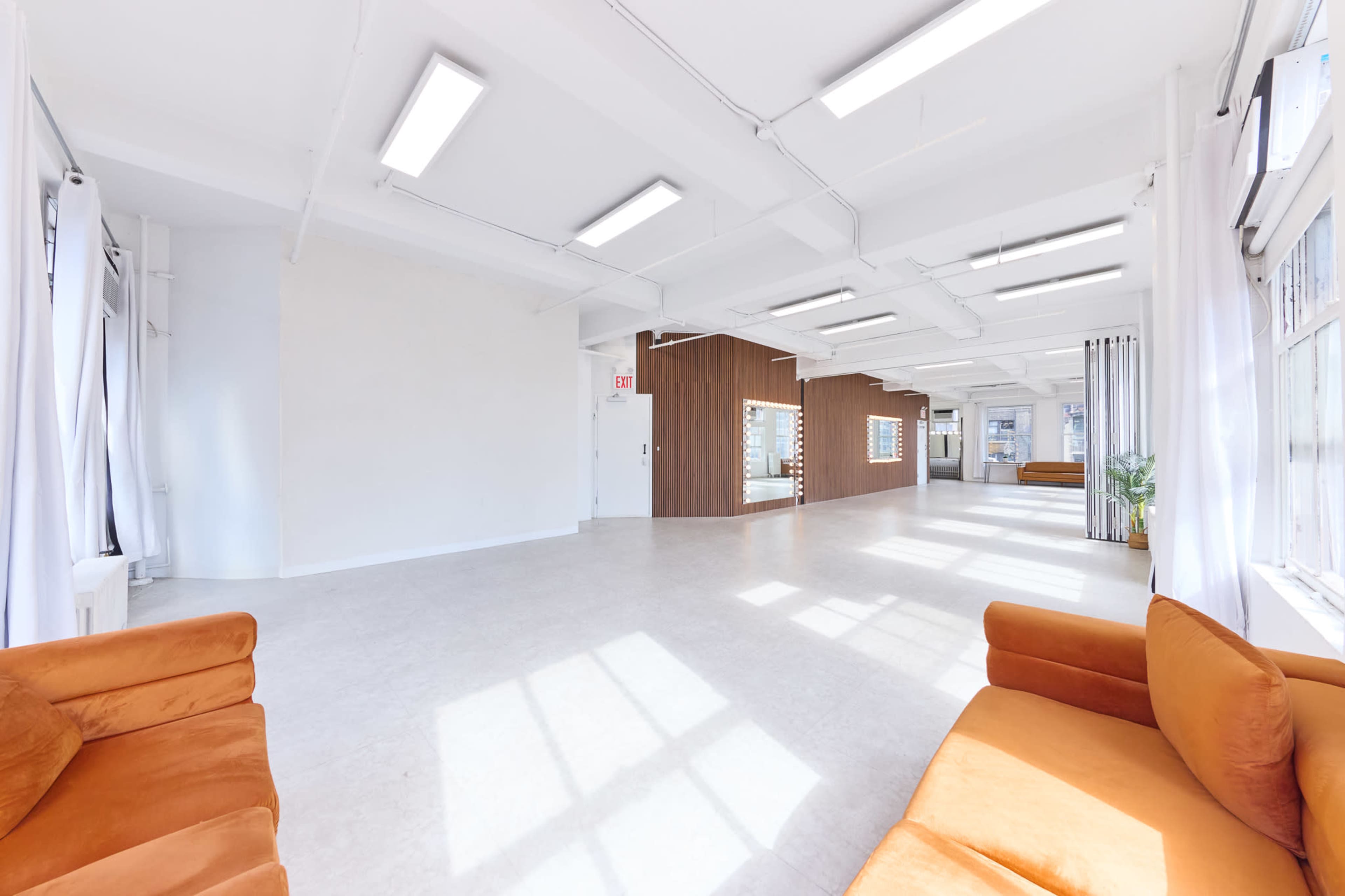 The image shows a spacious, well-lit interior with a light-colored floor, orange sofas, and mirrored walls.