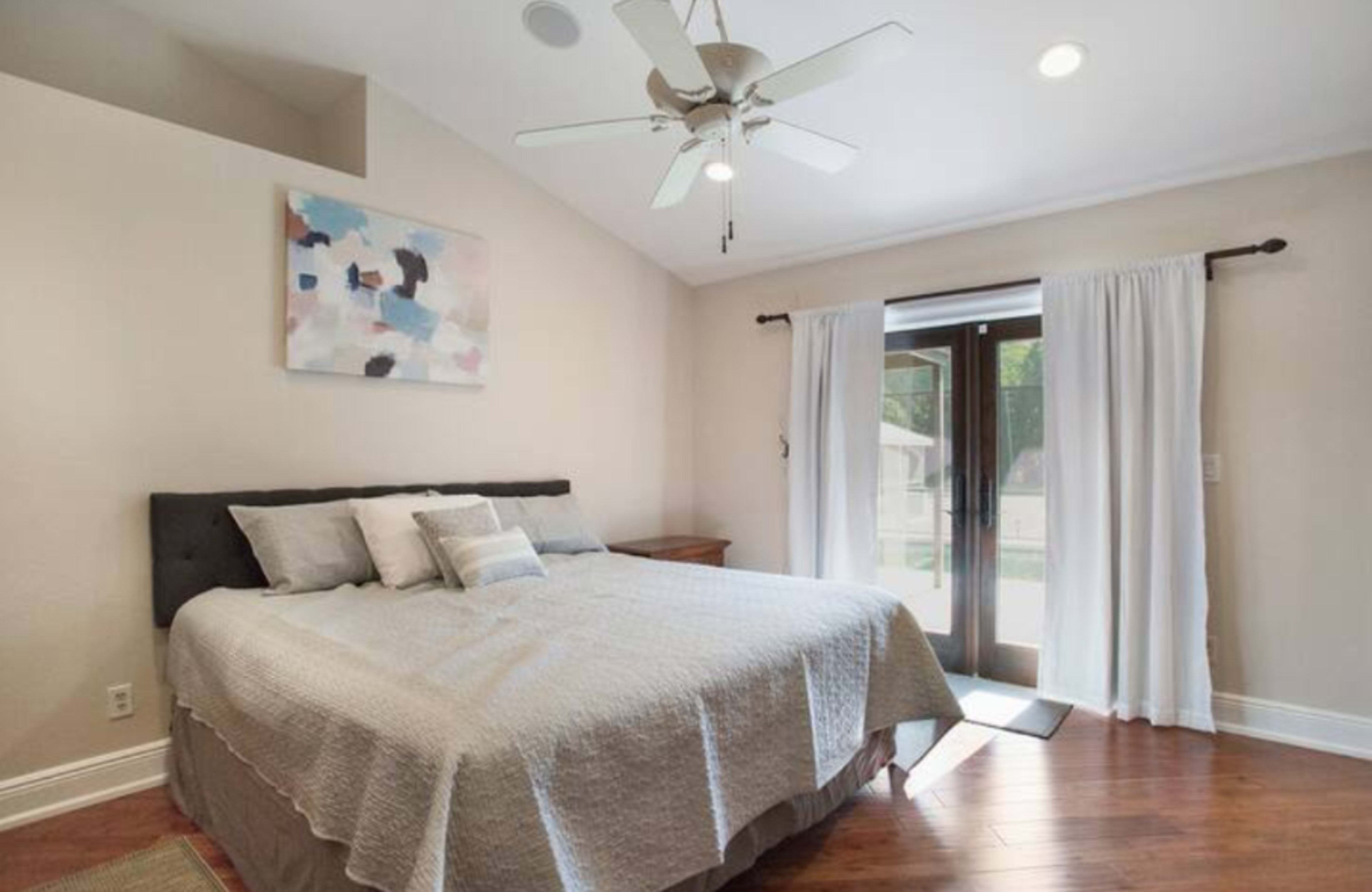 A bedroom features a large bed with light bedding, a wooden nightstand, and French doors leading to an outdoor area.