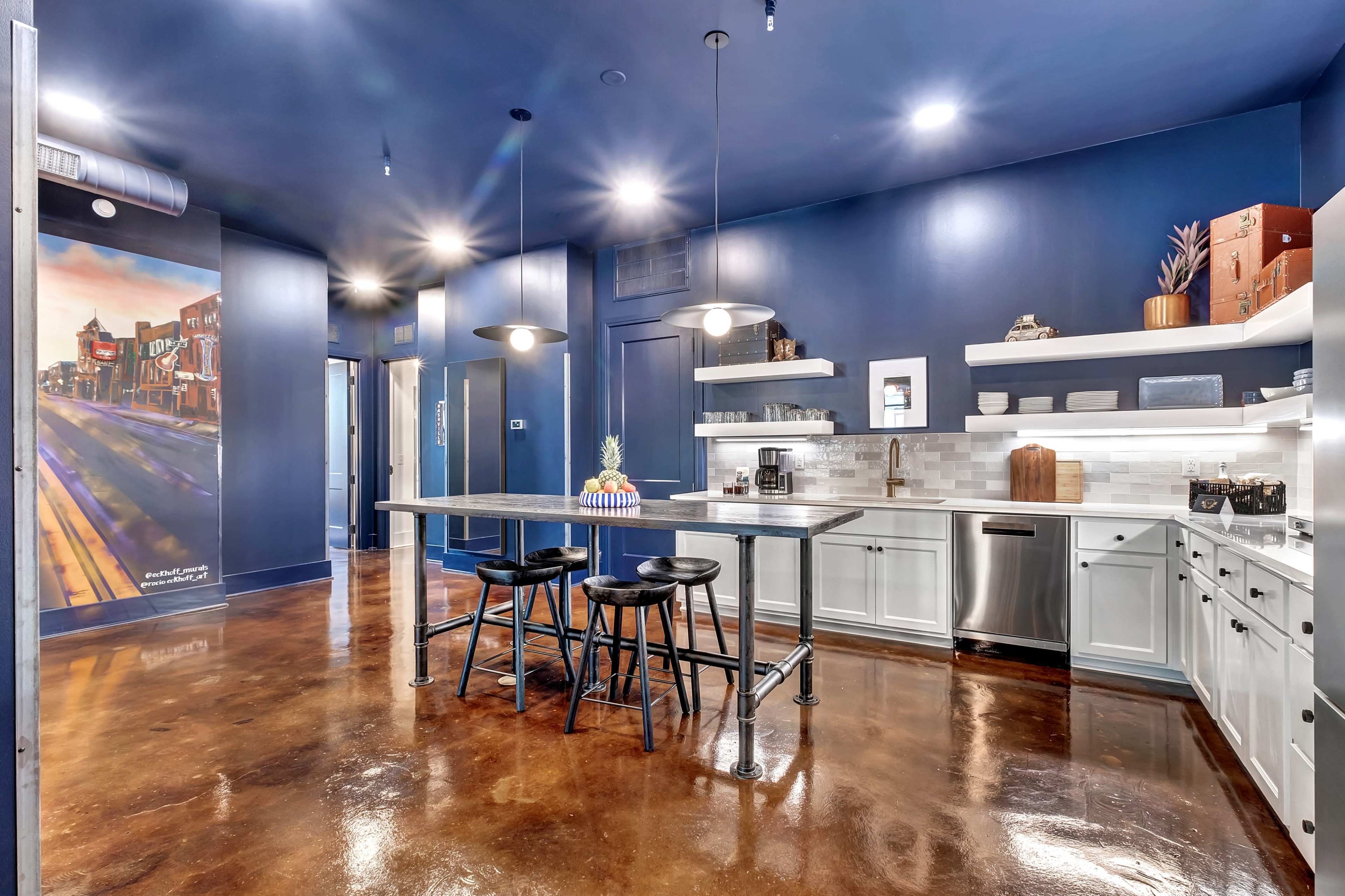 The image shows a modern kitchen with dark blue walls, white cabinetry, a large island with bar stools, and stainless steel appliances.