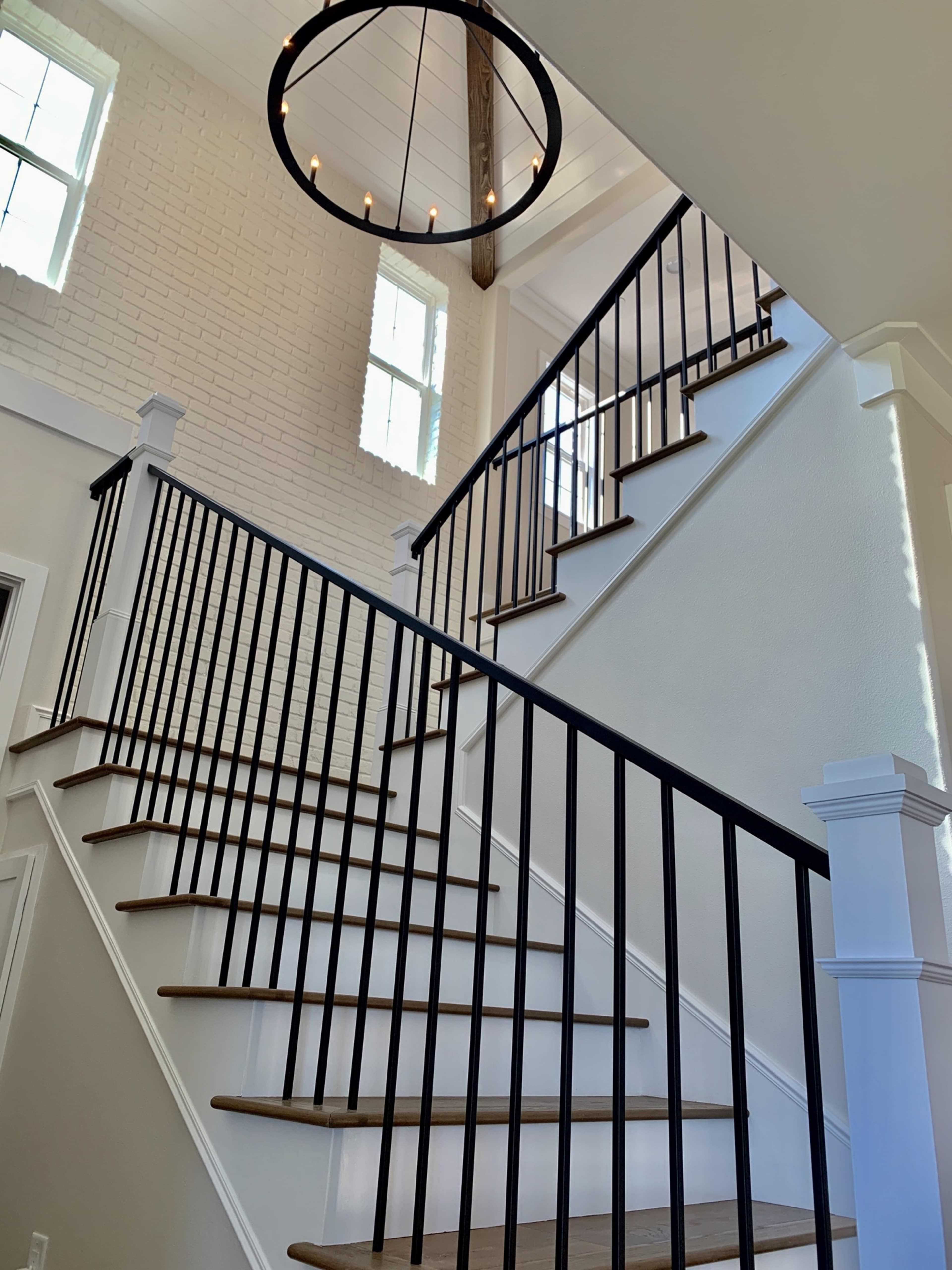 A stairway with wooden steps and black railings, illuminated by a circular chandelier overhead.