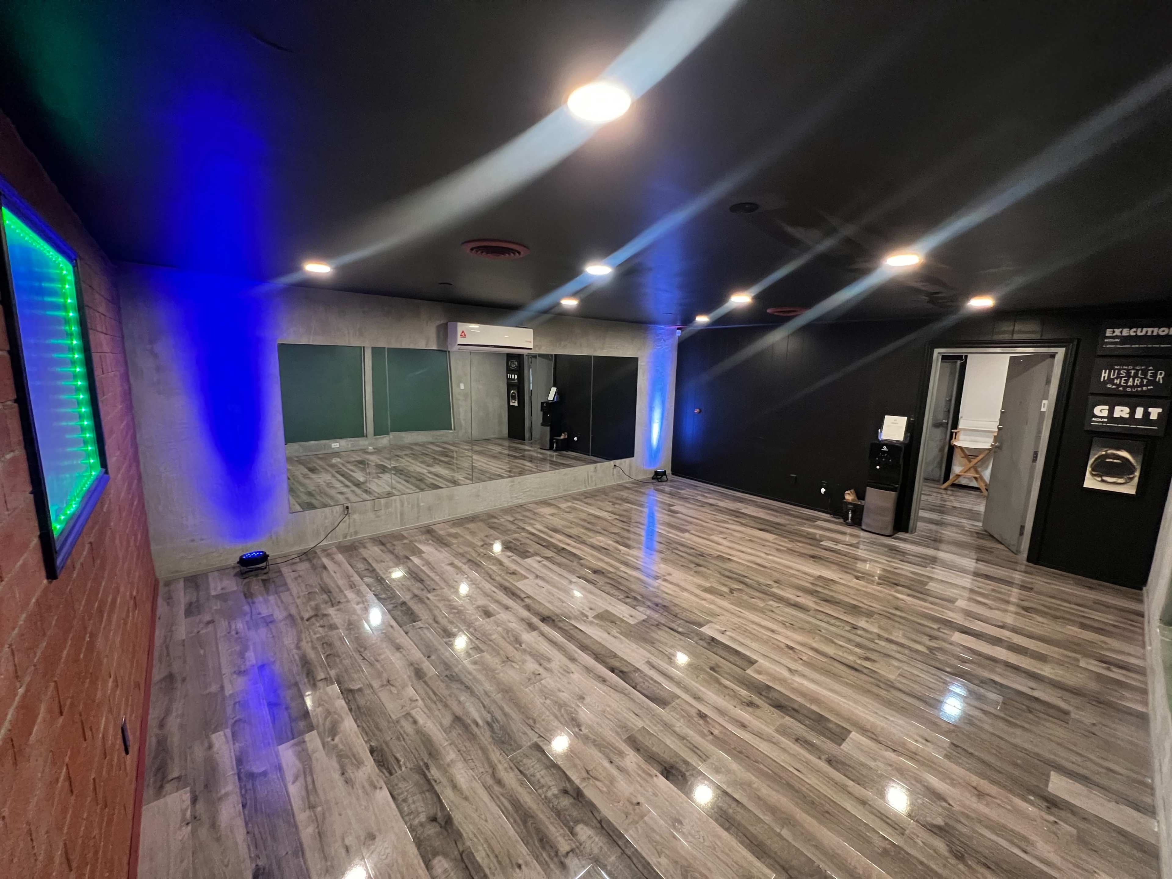 A spacious room with polished wooden floors, a large mirror on one wall, and blue and green lighting accents.