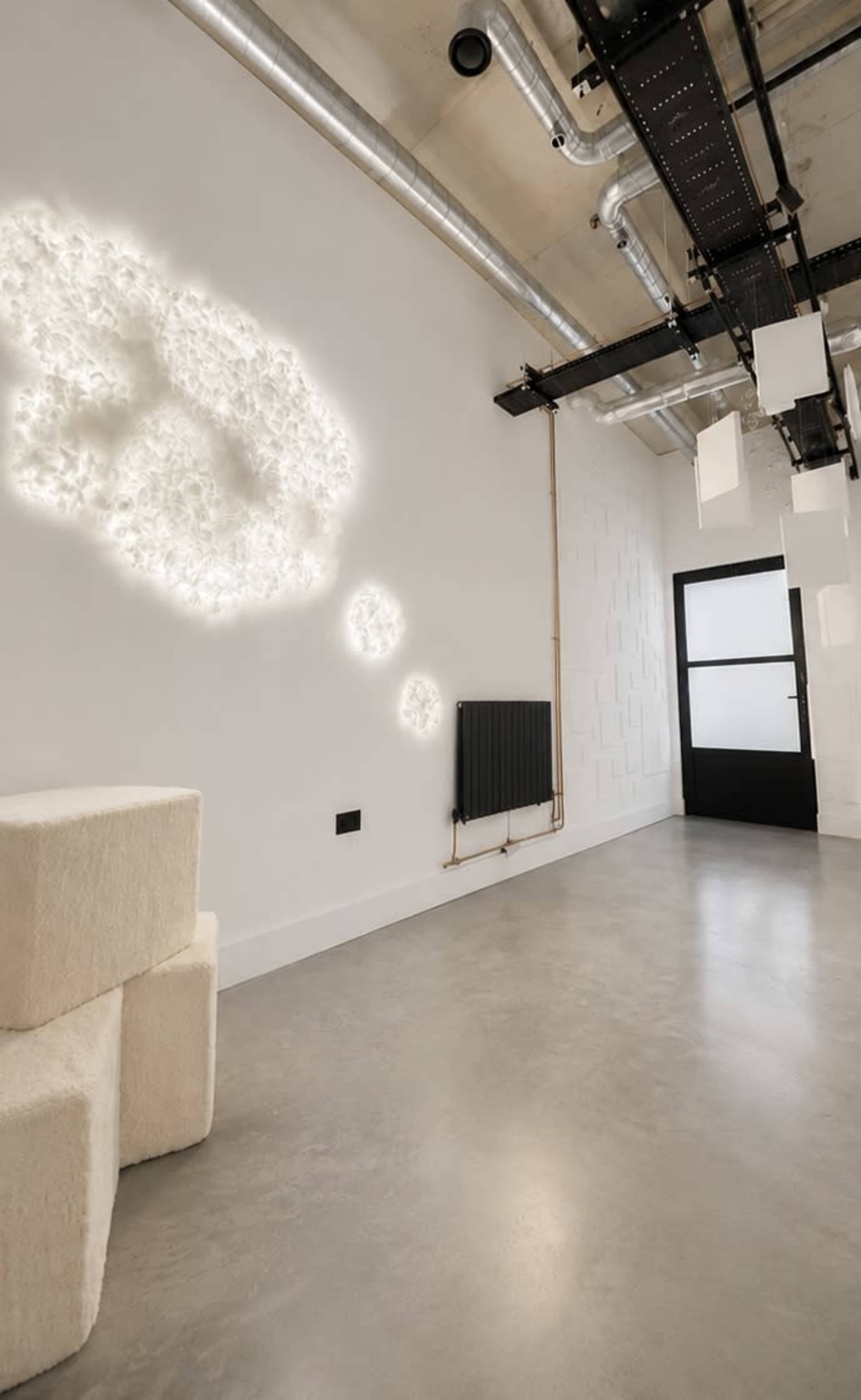The interior features a minimalist space with a textured wall displaying illuminated cloud-like shapes and a radiator beside a door.