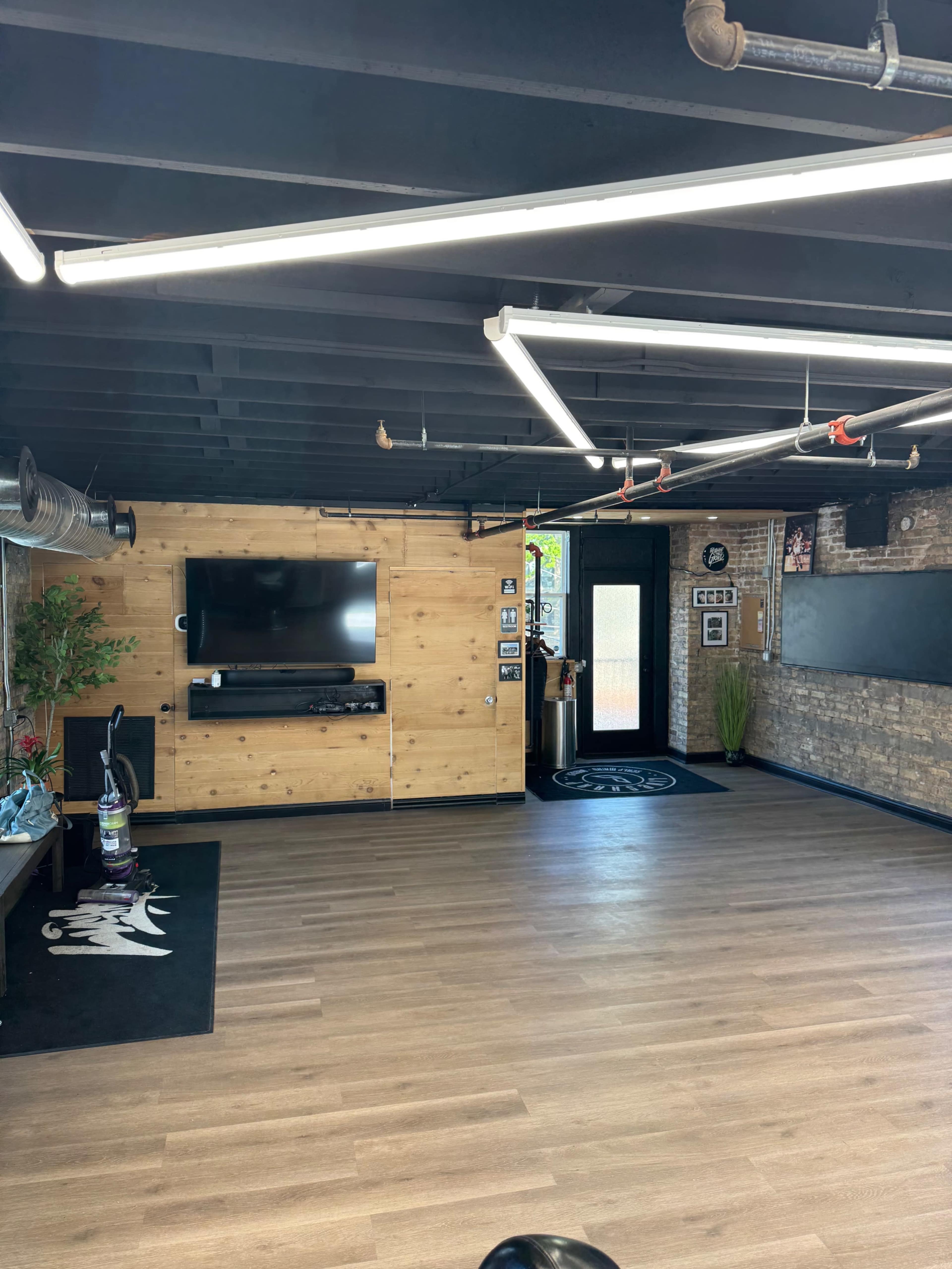 The interior of a modern commercial space features wooden paneling, a TV mounted on the wall, and a large glass door, with a polished floor and minimal furnishings.