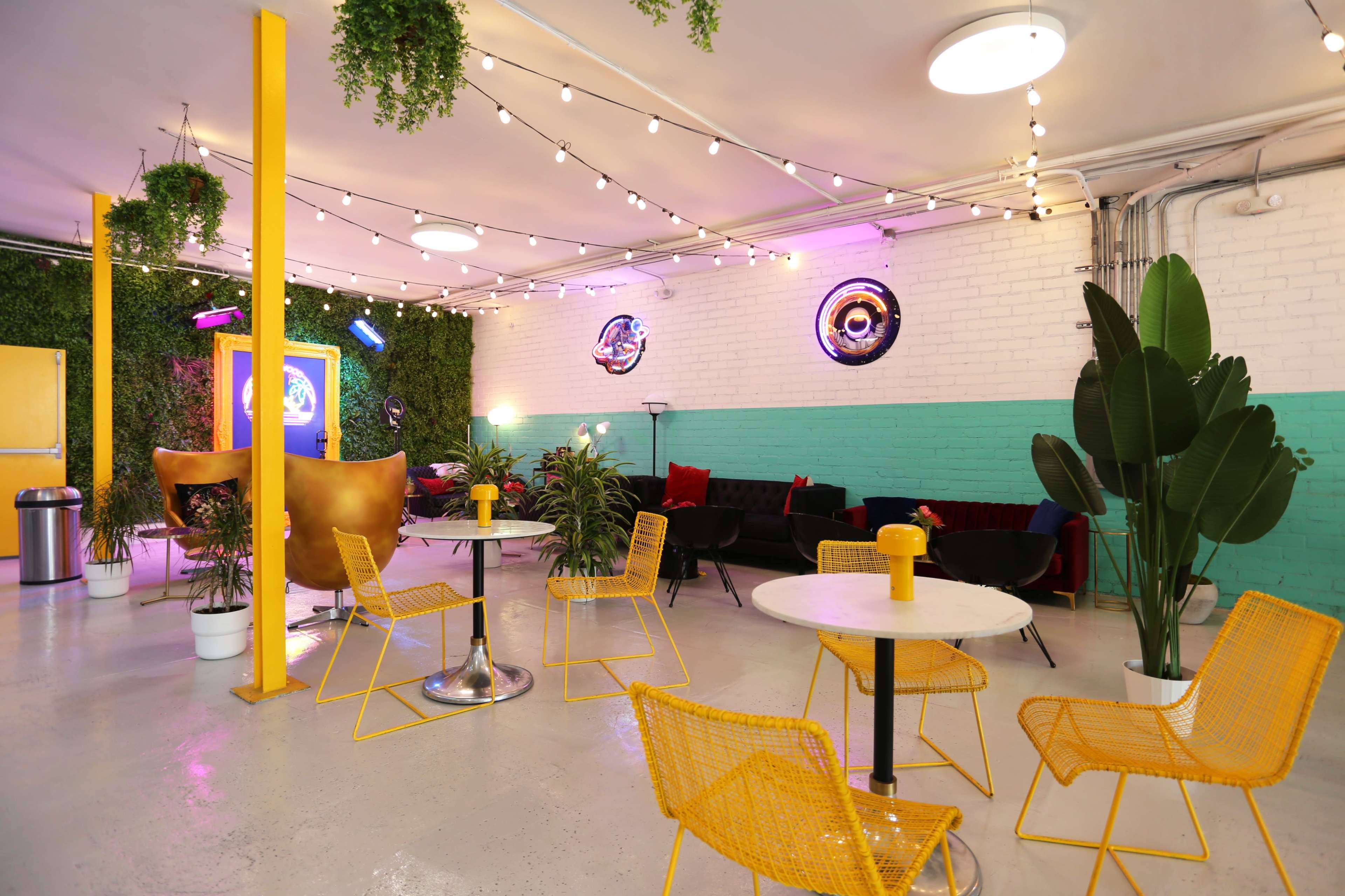 A brightly decorated indoor space with green plants, colorful furniture, and string lights.