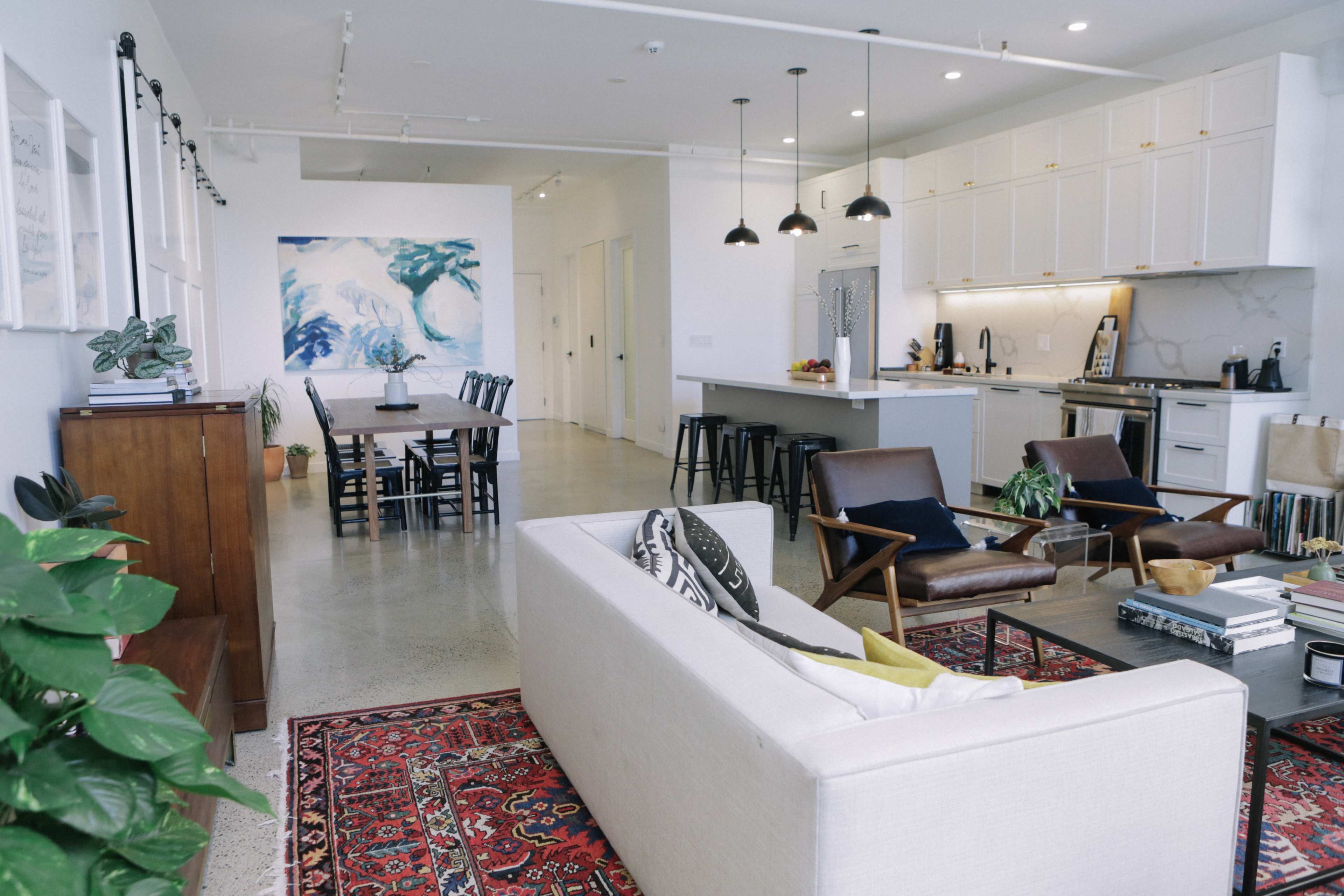 A spacious, modern living area and dining space, featuring a sofa, dining table, and kitchen with elegant cabinetry and industrial-style lighting.