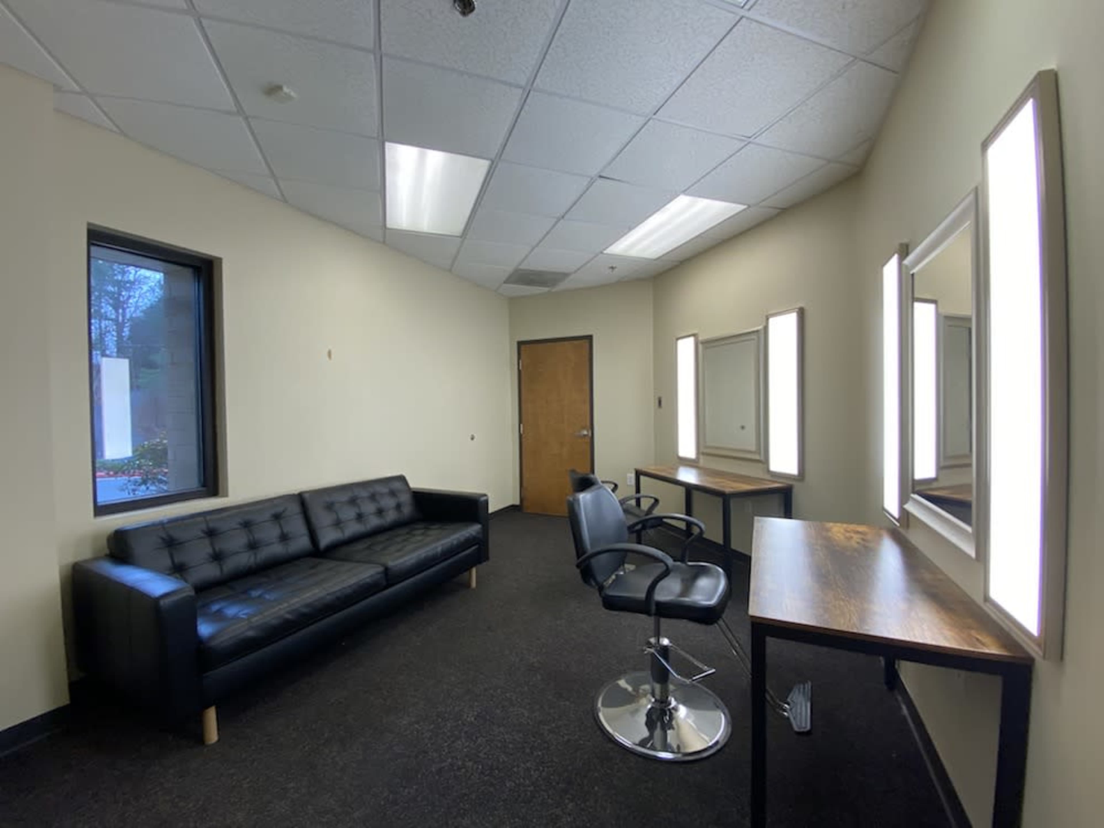 A minimalist room with a black sofa, a salon chair, and two well-lit mirrors mounted on the walls.