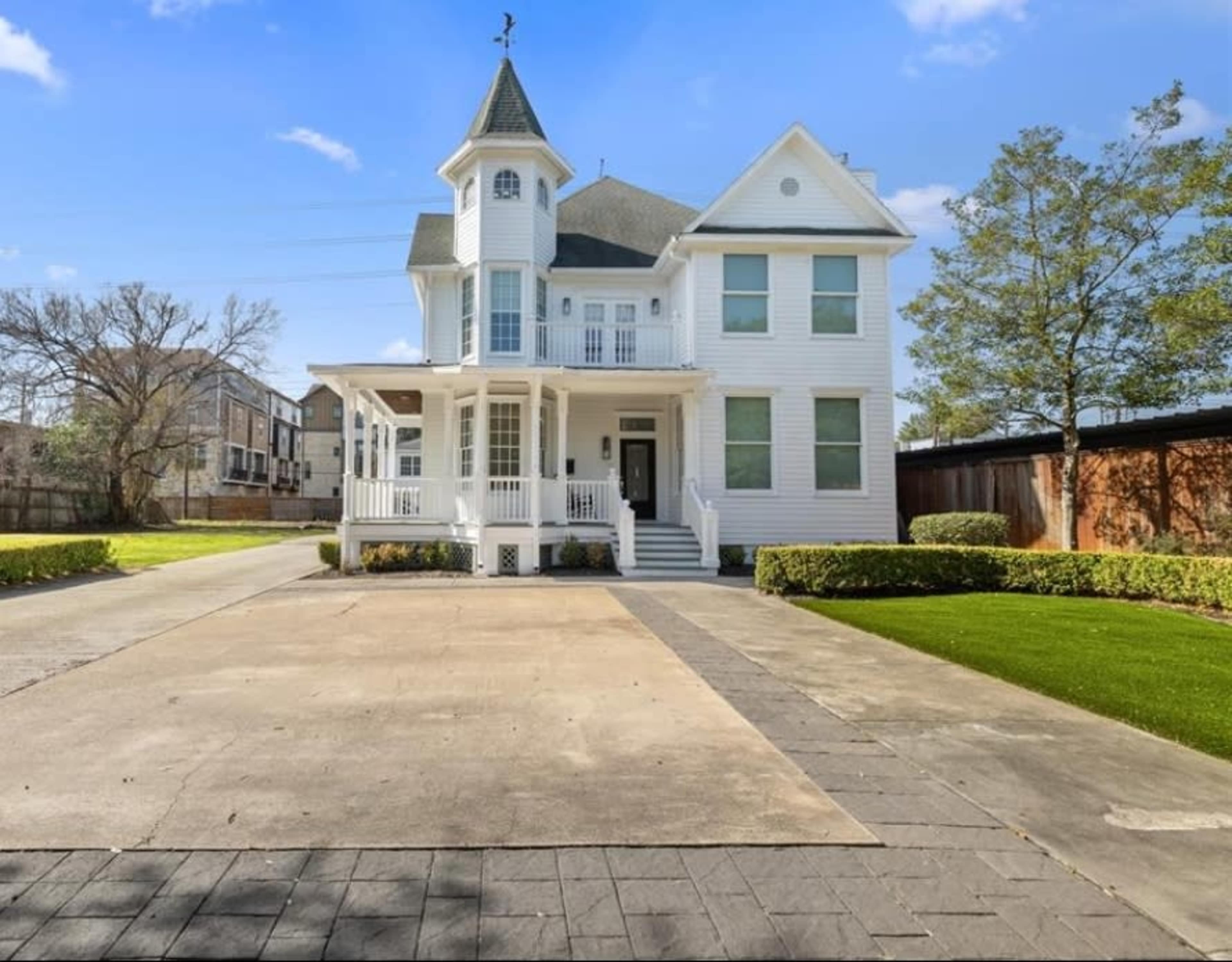 A large, two-story white Victorian-style house with a tower, a covered porch, and a paved driveway.