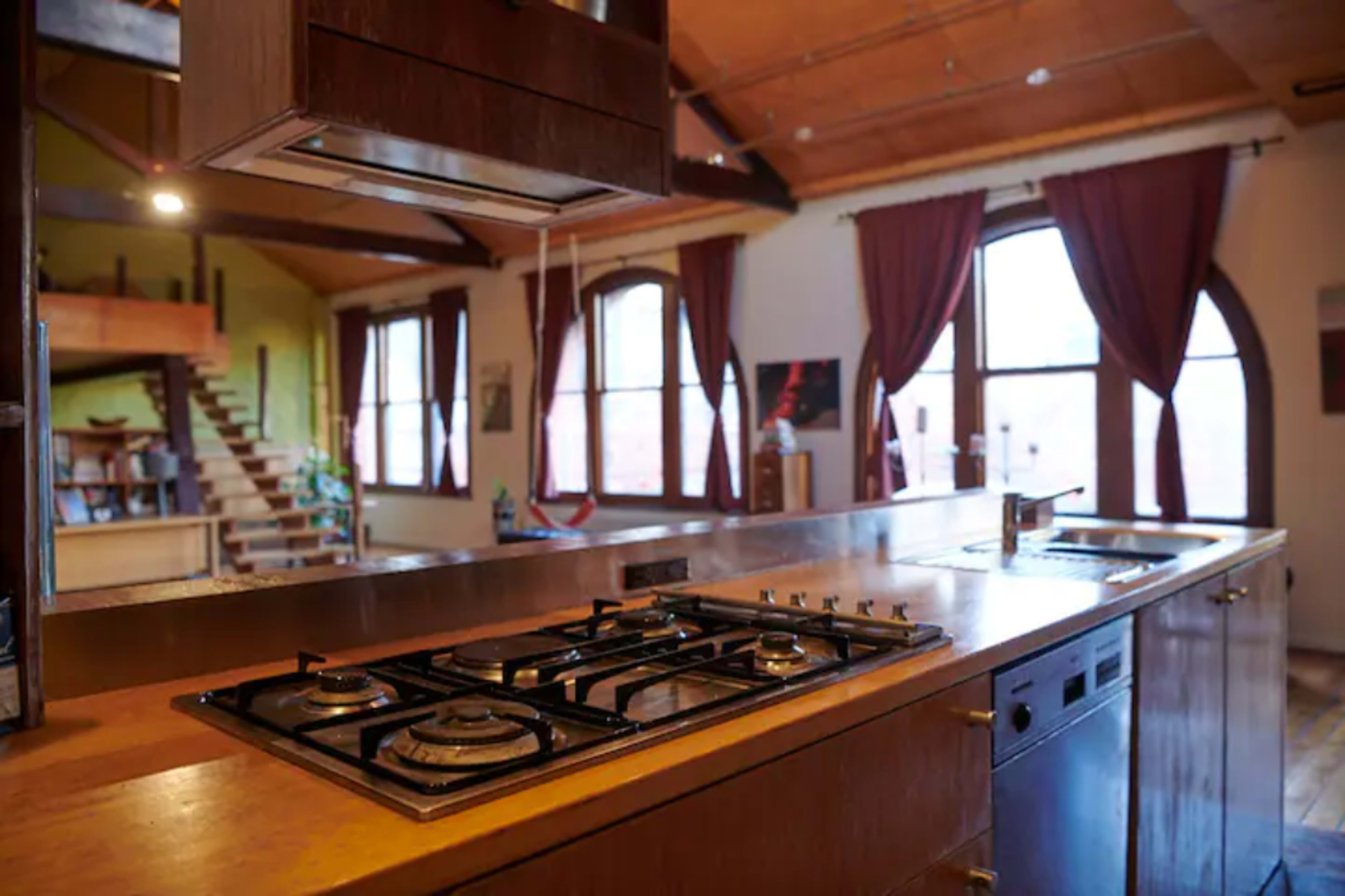 A modern kitchen with a gas stove, a stainless steel countertop, and large windows framed by curtains.