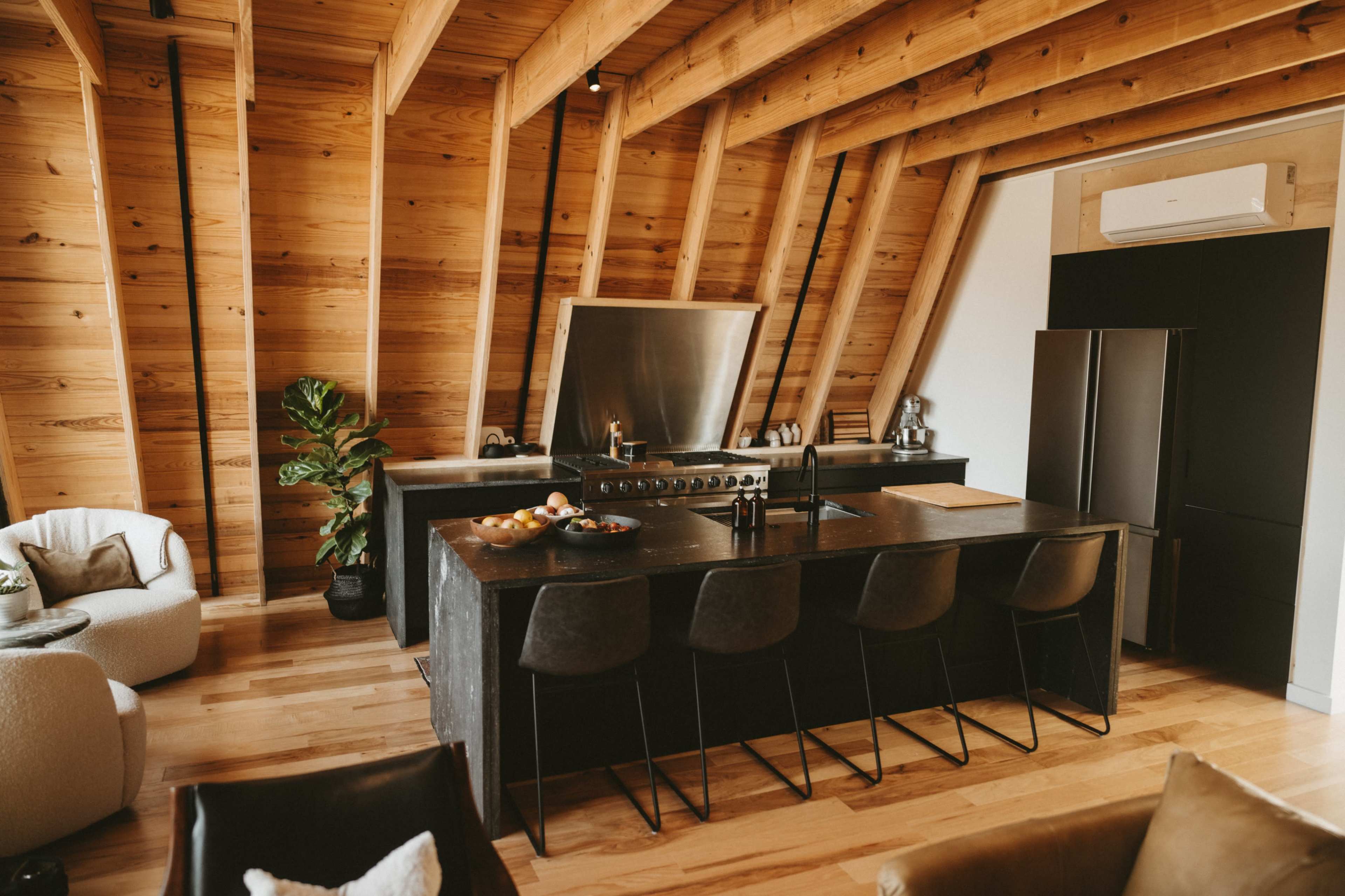 A modern kitchen features a large black island with bar seating, stainless steel appliances, and wooden beams in the ceiling.