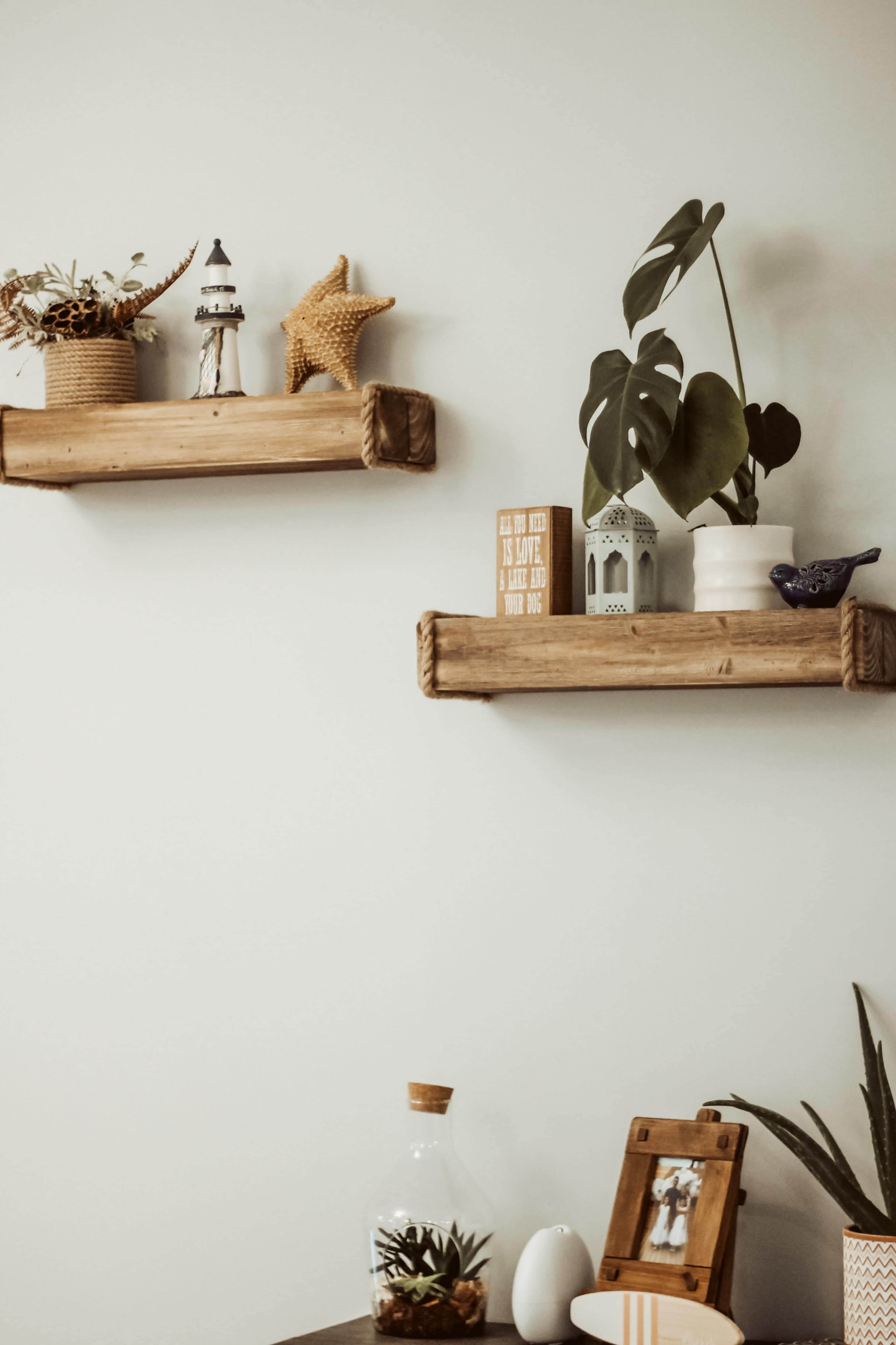 Two wooden shelves display decorative items, including a lighthouse, a starfish, plants, and small ornaments against a light wall.