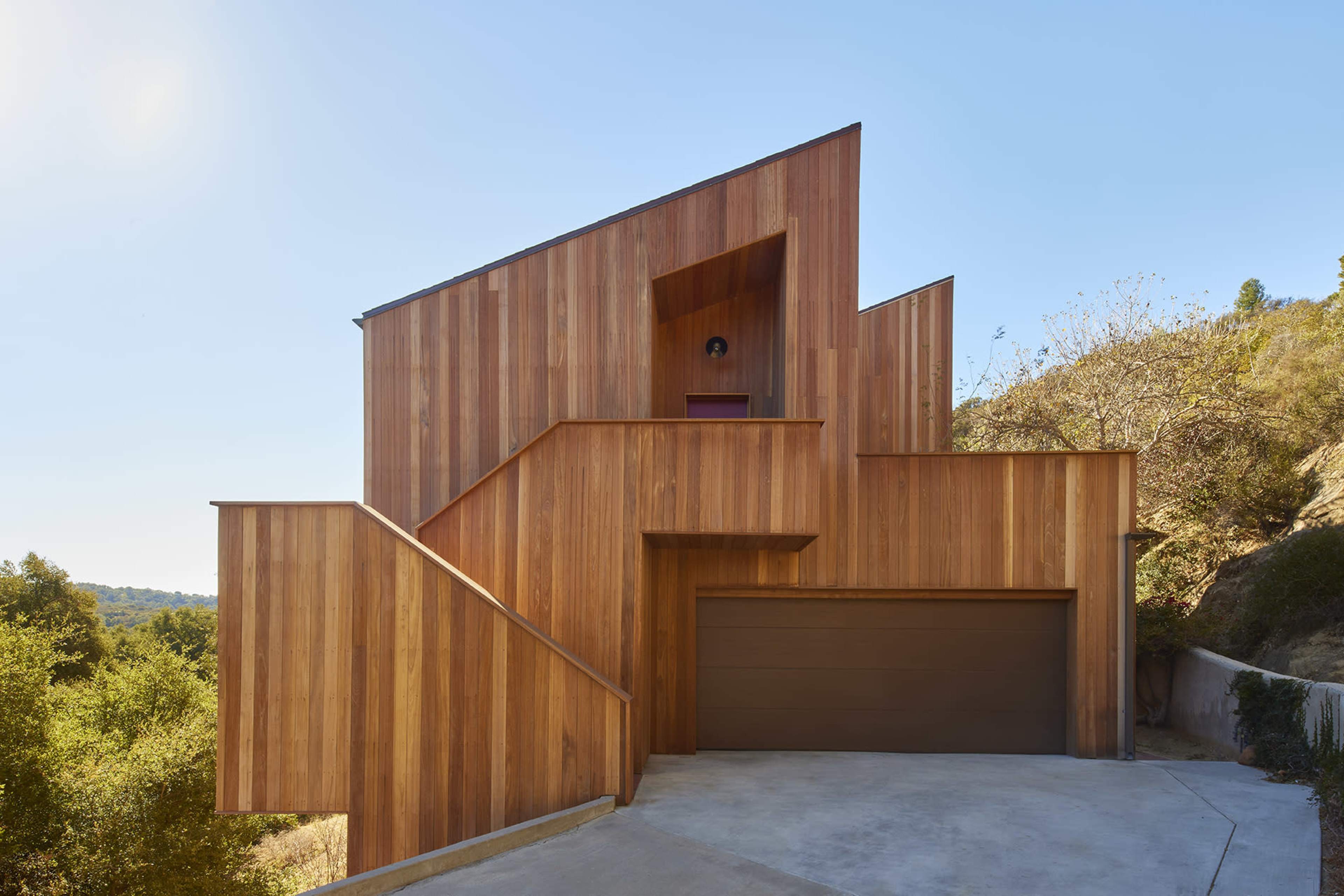 A modern wooden house with a geometric design, featuring slanted walls and a garage at the base.