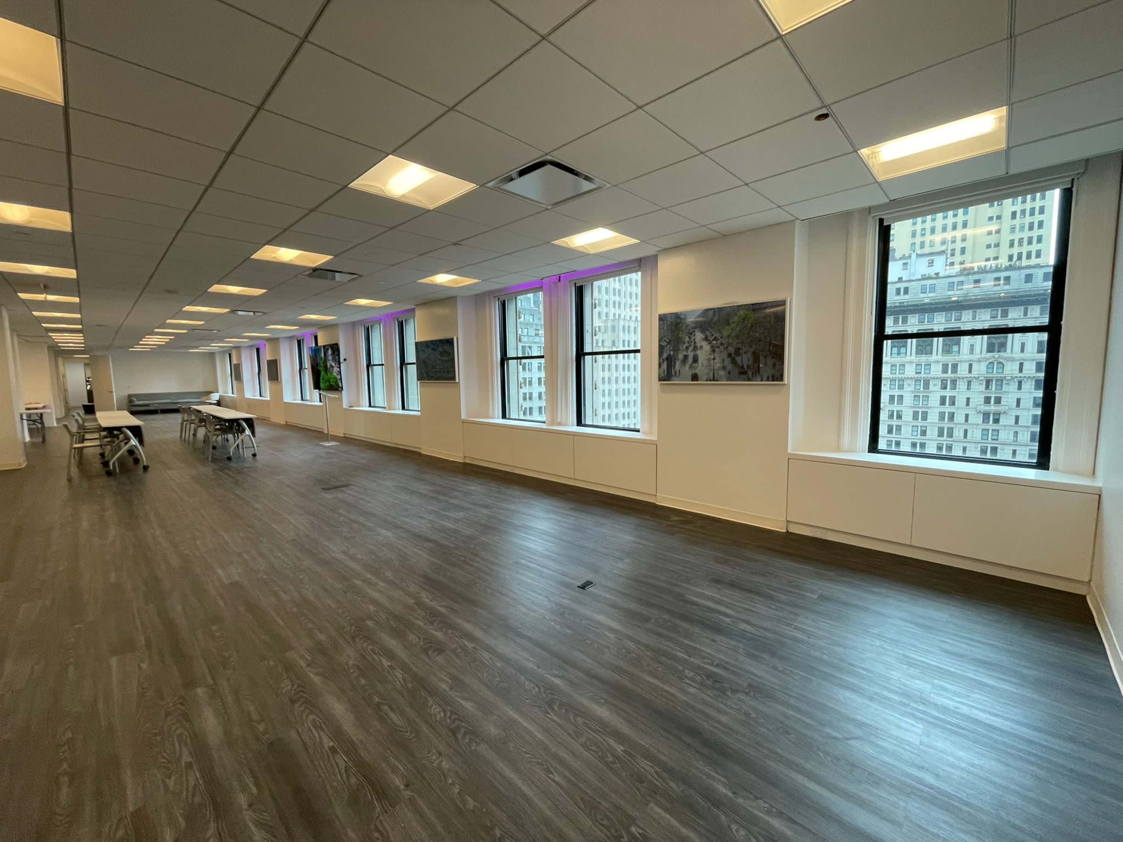 The image shows a spacious, well-lit office interior with multiple windows and wooden flooring.