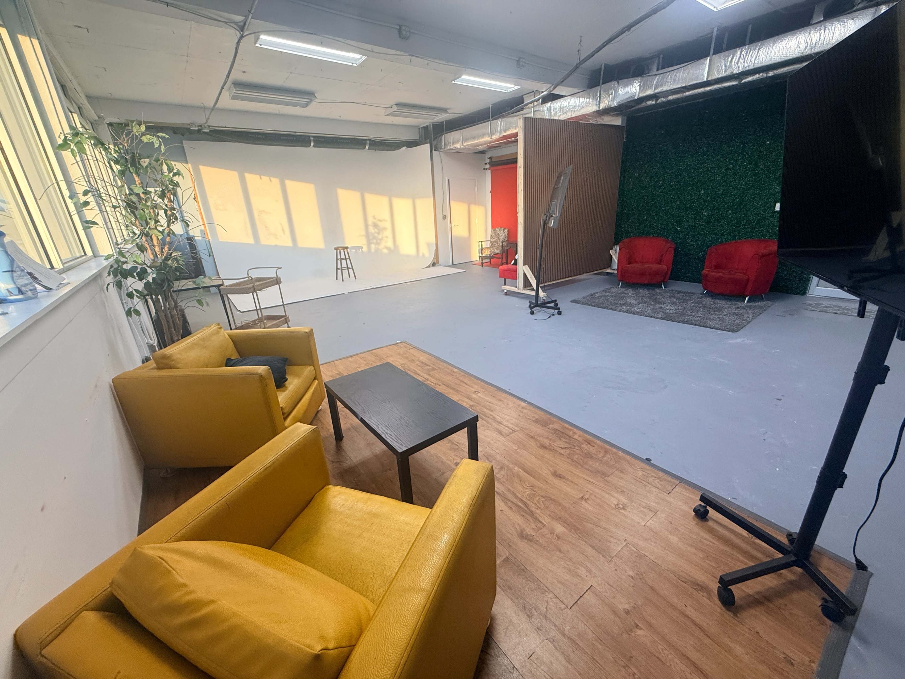 The image shows a spacious studio with yellow armchairs, a small black table, and a backdrop featuring two red chairs against a green wall.