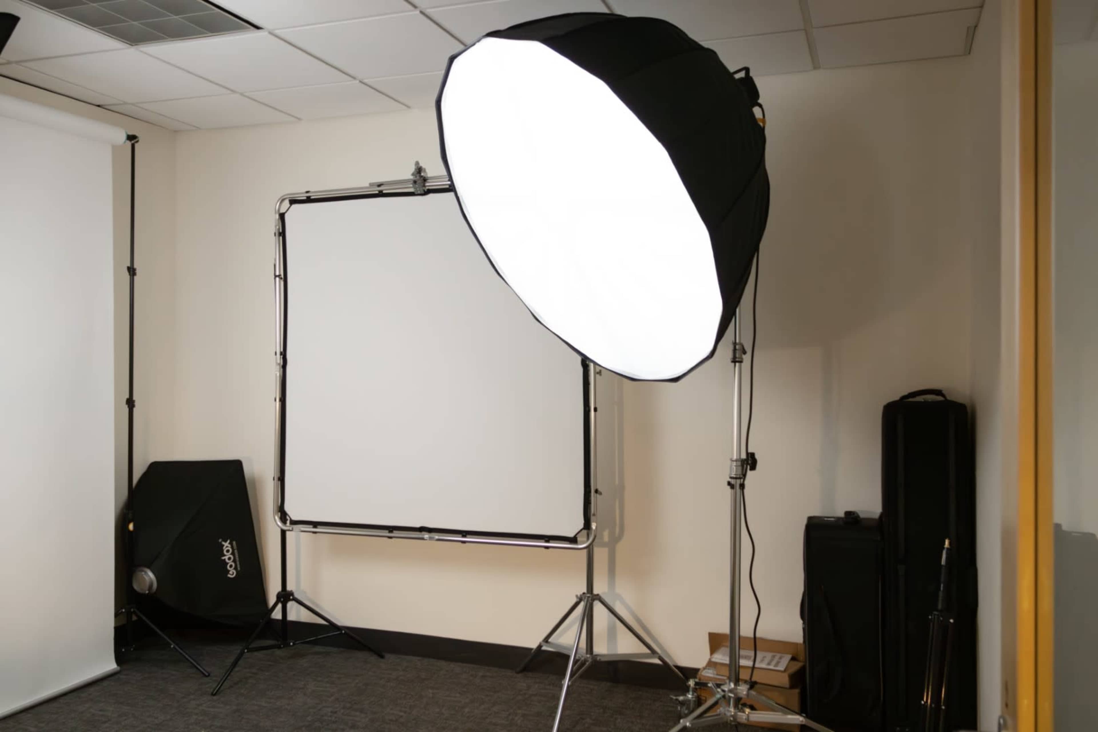 A studio setup featuring a large softbox light, a backdrop, and various photography equipment.