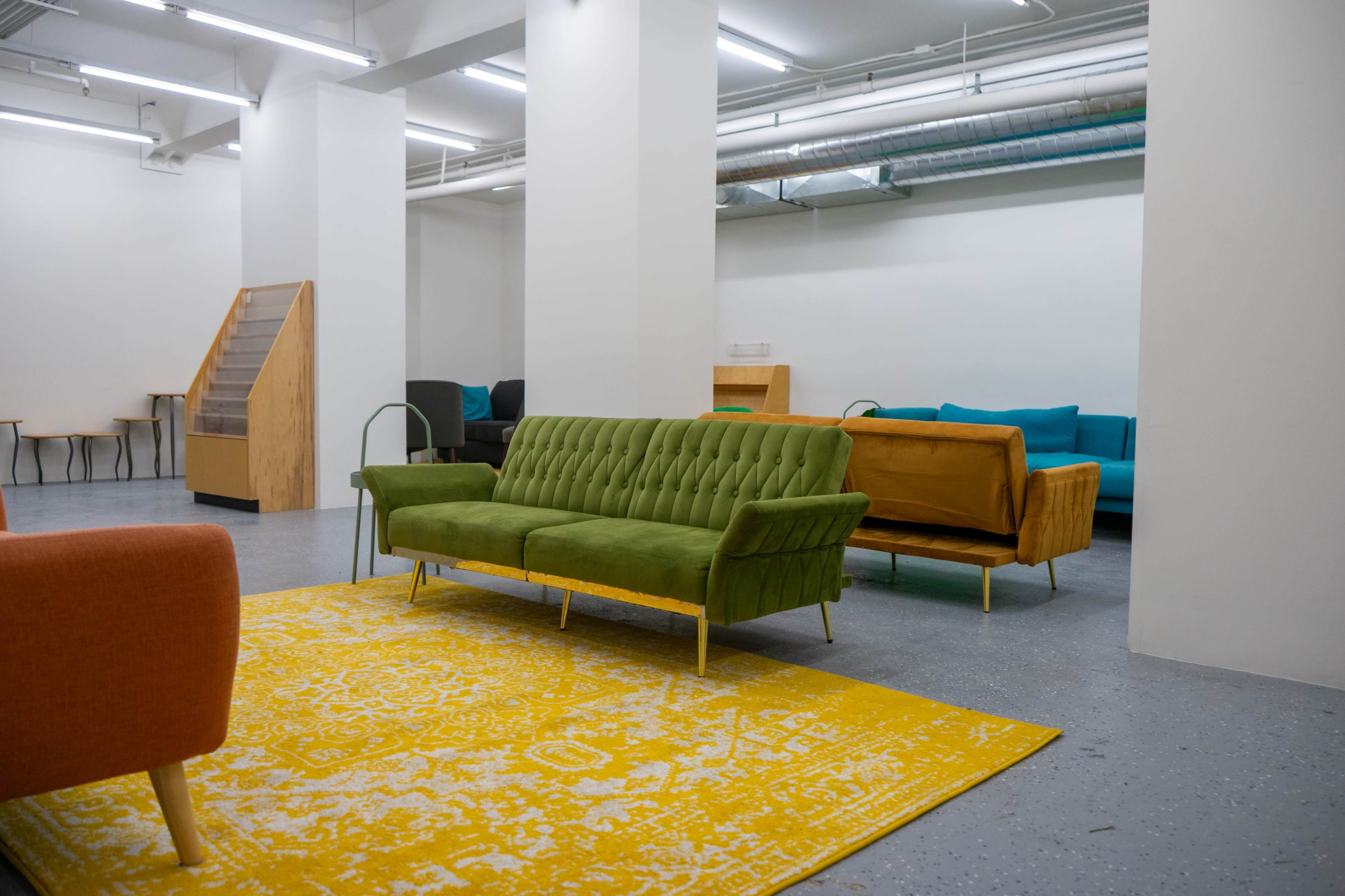 The image shows a spacious room with multiple couches in various colors and a large yellow and white area rug on the floor.