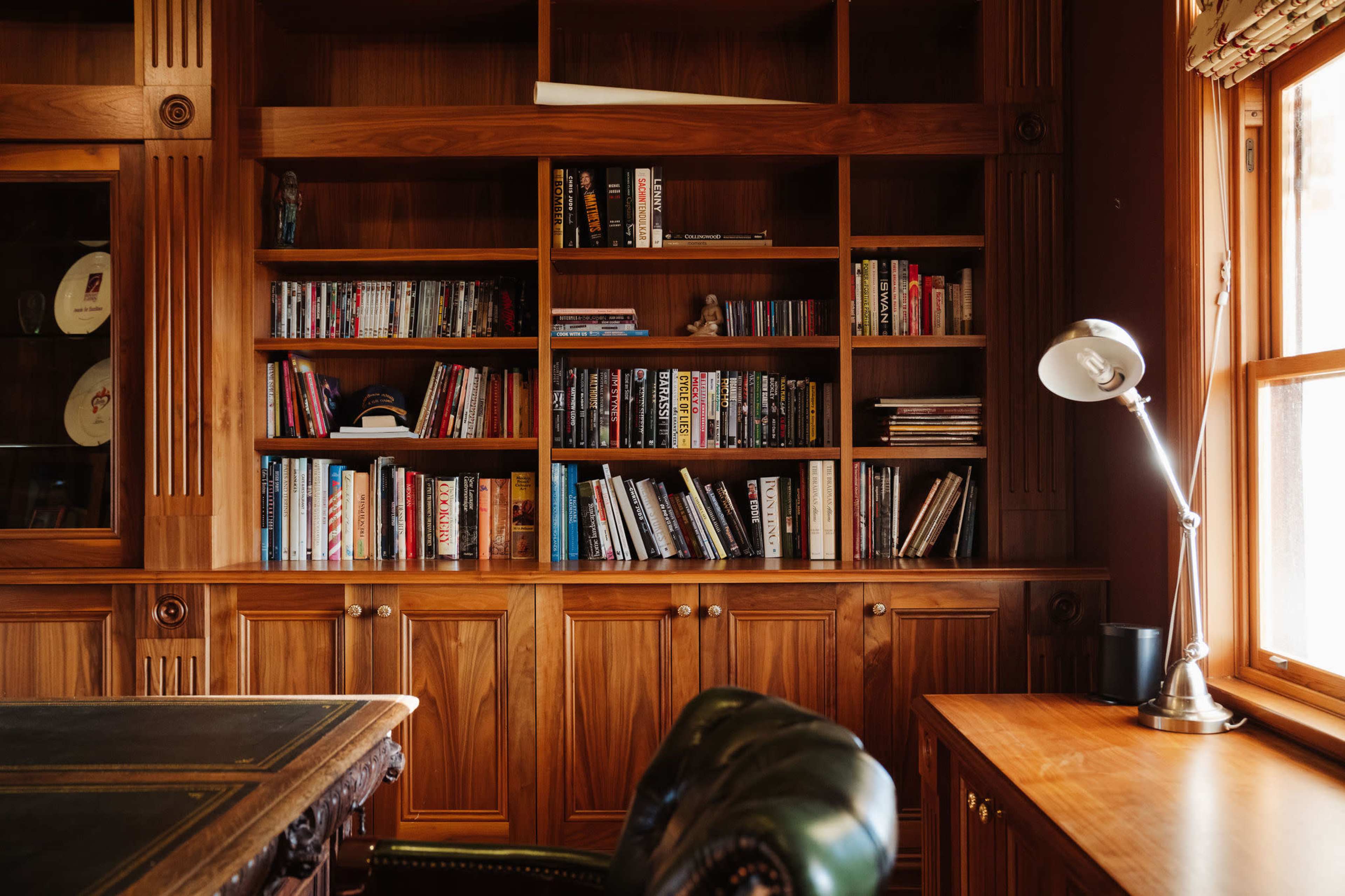 The image shows a wooden bookshelf filled with various books, accompanied by a desk and a lamp in a well-organized office space.