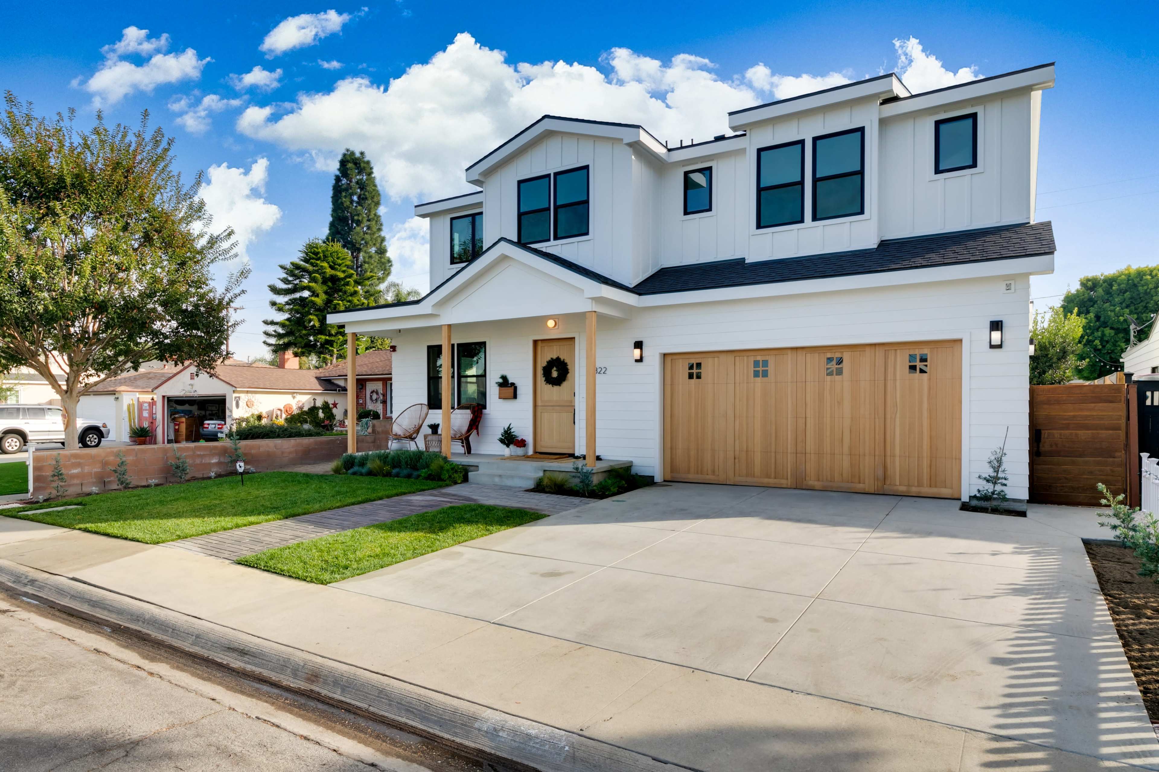 A modern two-story house with a wooden garage door, a front porch, and a neatly landscaped yard.