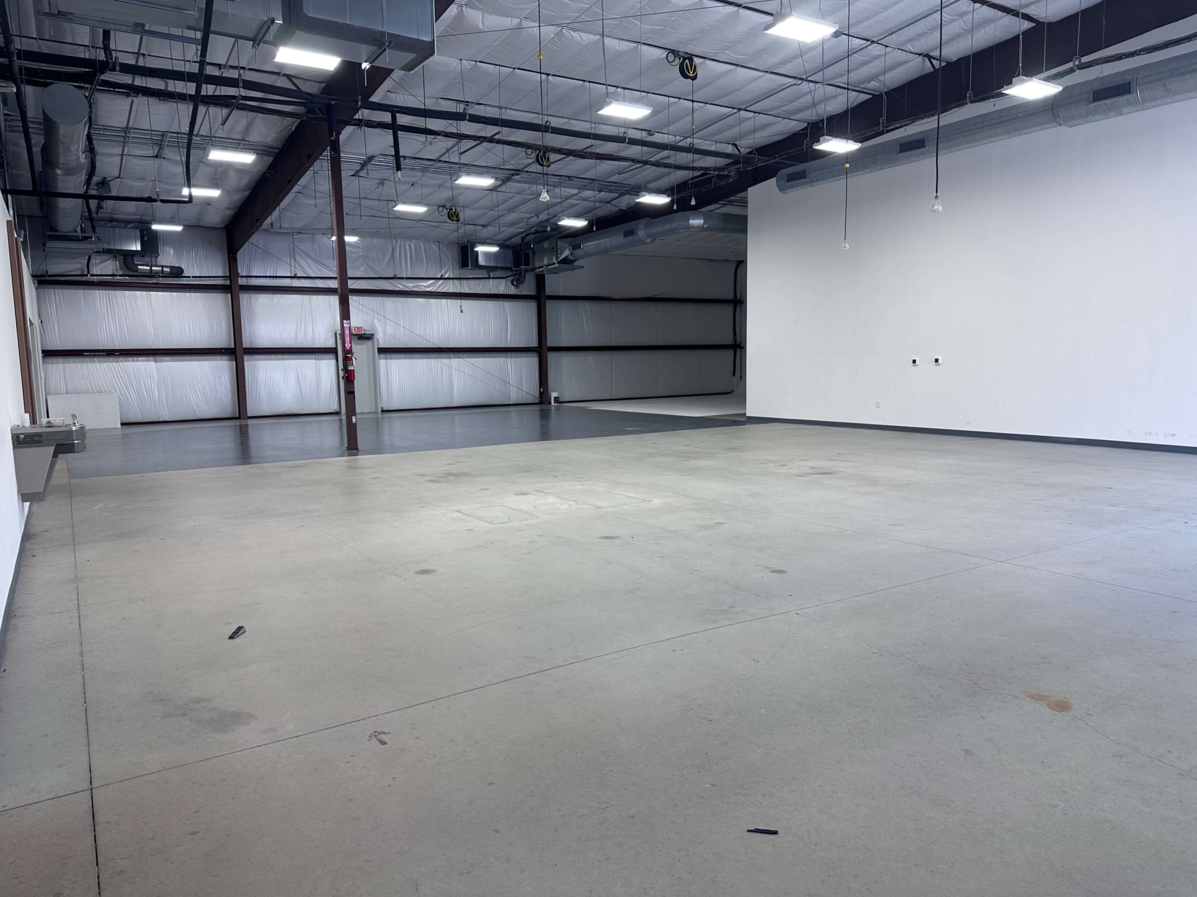 The image shows an empty industrial warehouse space with concrete flooring and metal beams.