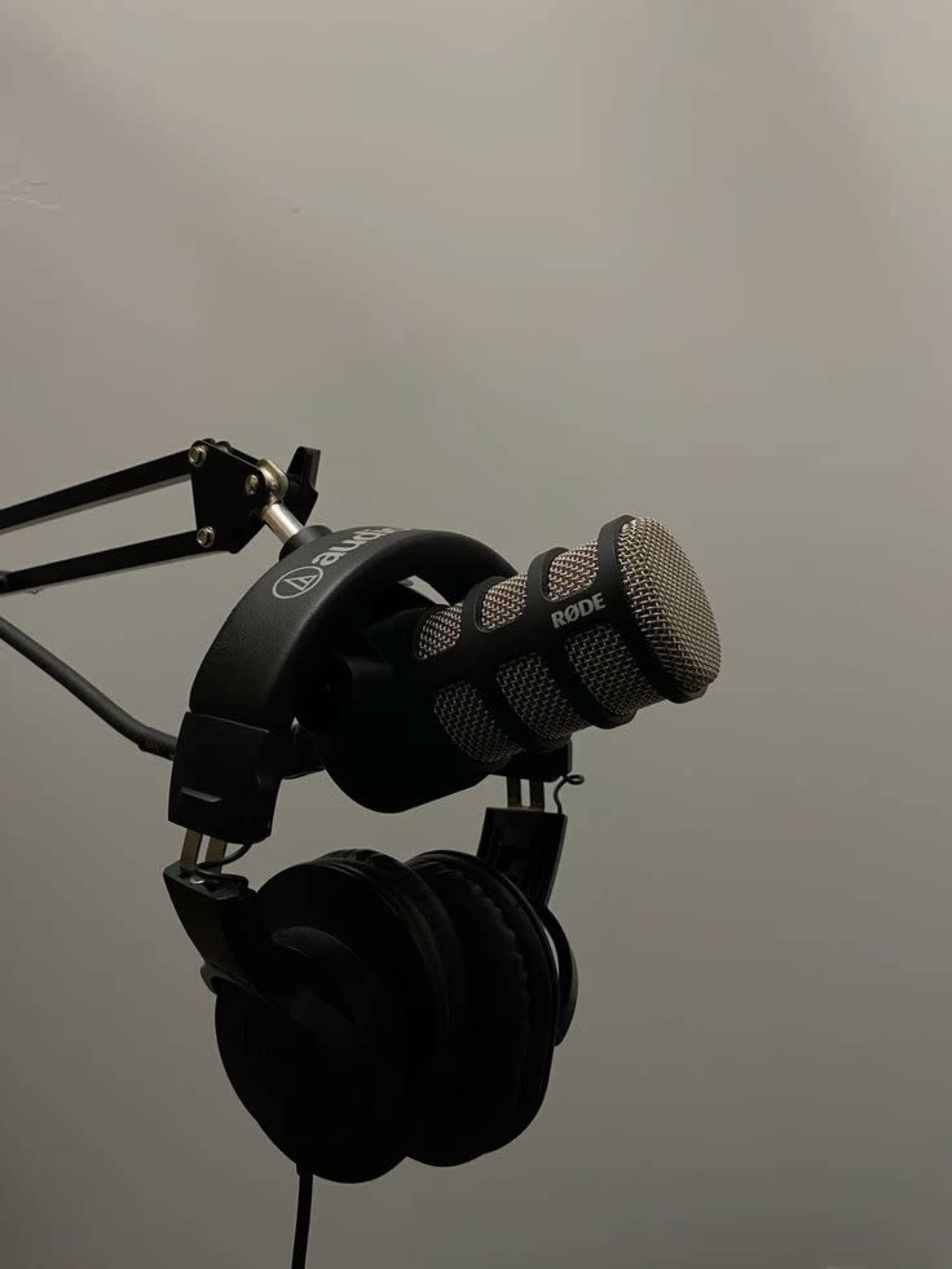 A microphone is mounted on a stand with a pair of black headphones hanging nearby against a gray background.