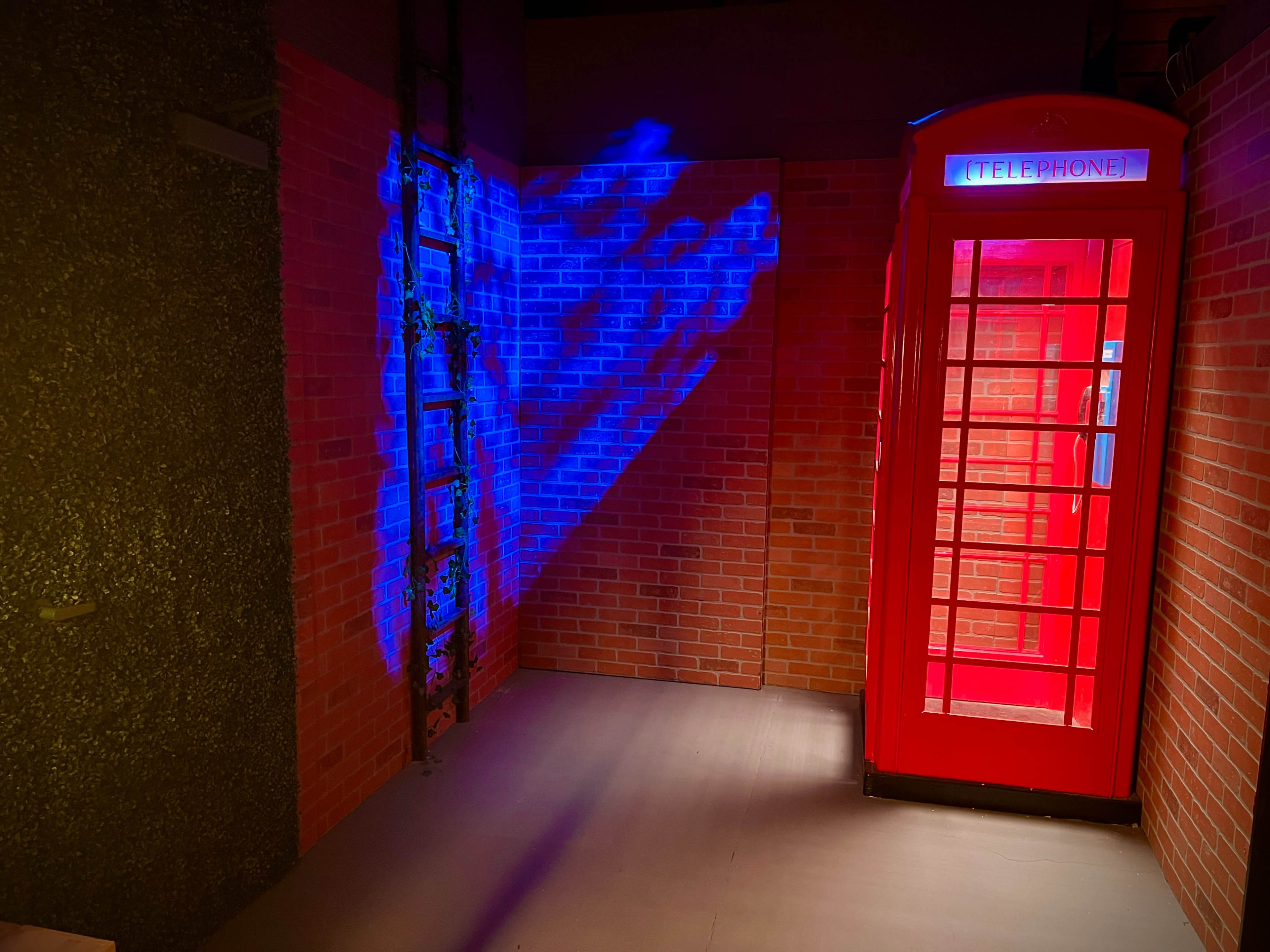 The image features a red telephone booth against a backdrop of brick walls, illuminated by blue and red lighting.