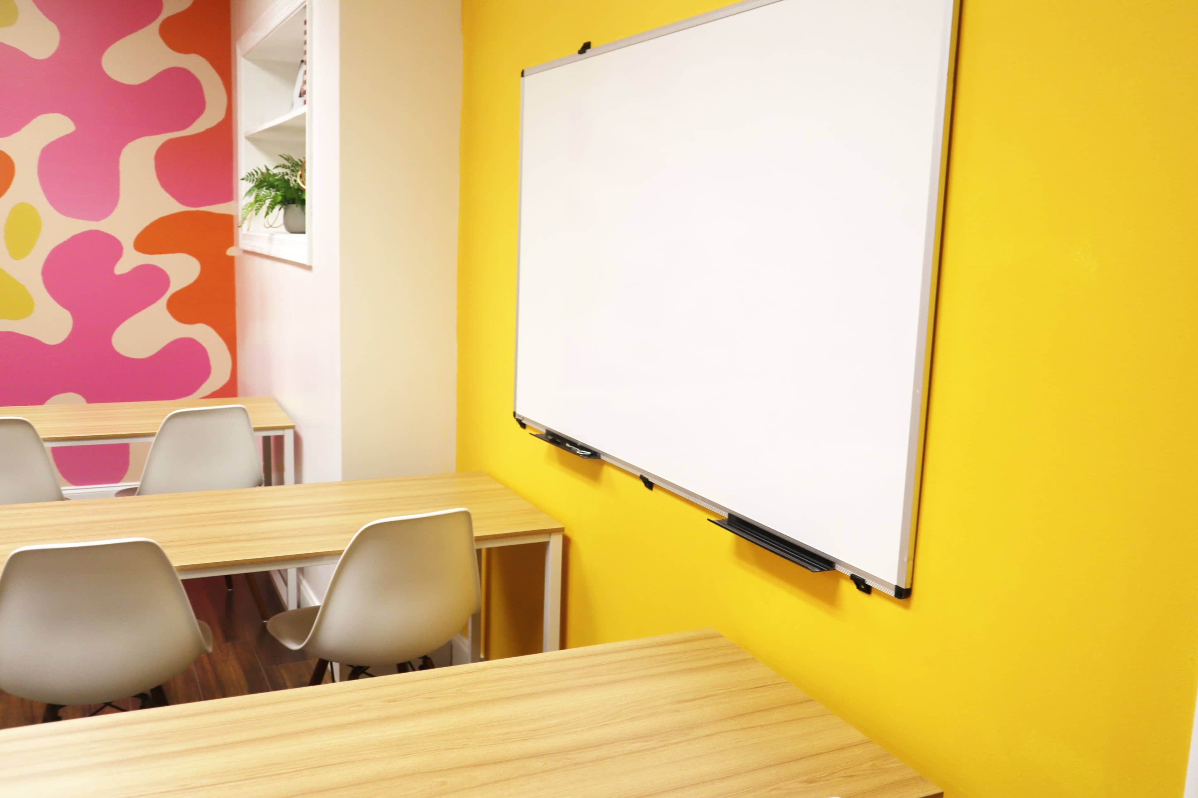 A classroom with yellow walls, a whiteboard, and wooden tables with white chairs.
