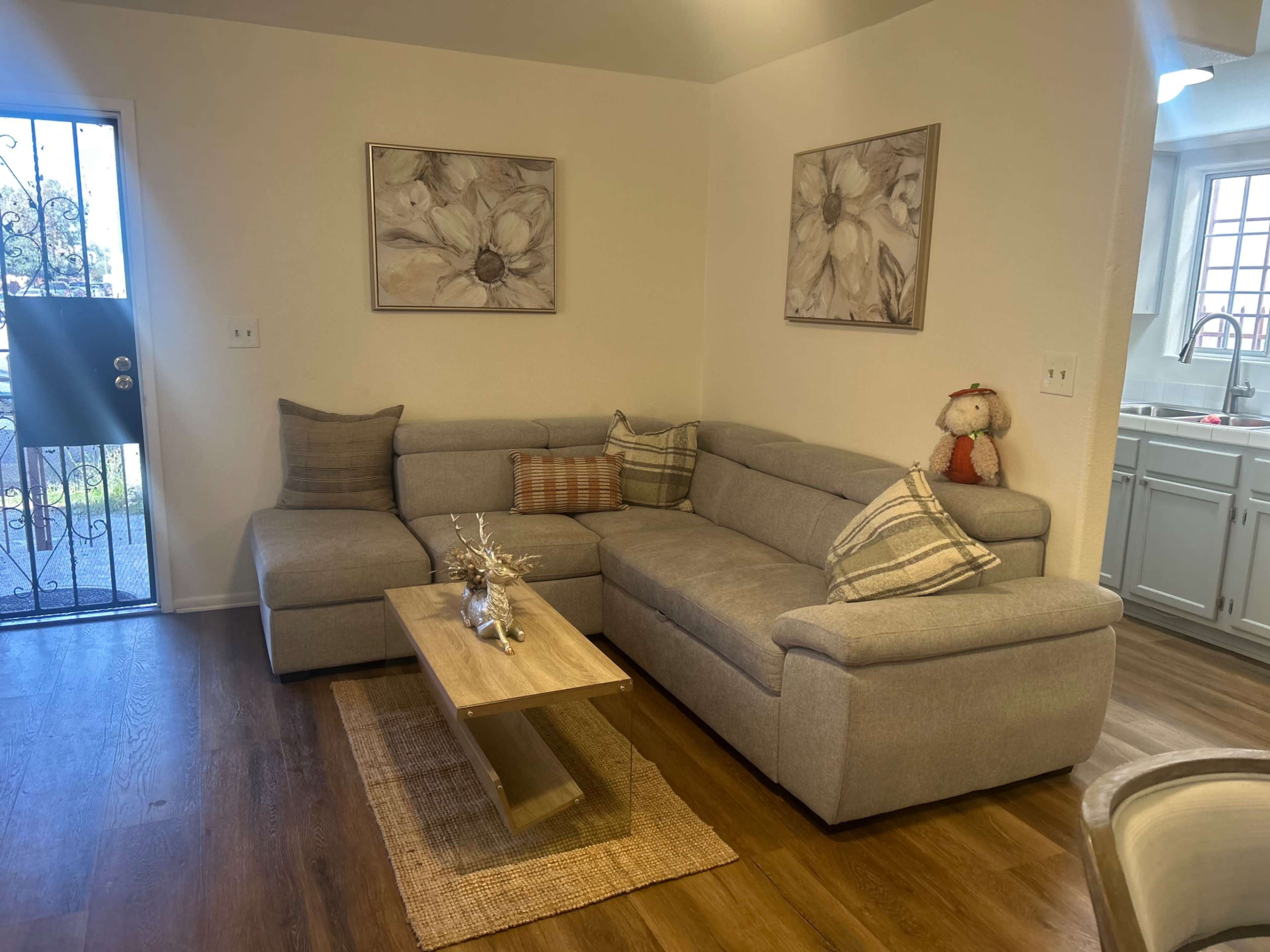 The image shows a modern living room with a gray sectional sofa, a wooden coffee table, and two floral wall artworks above the couch.