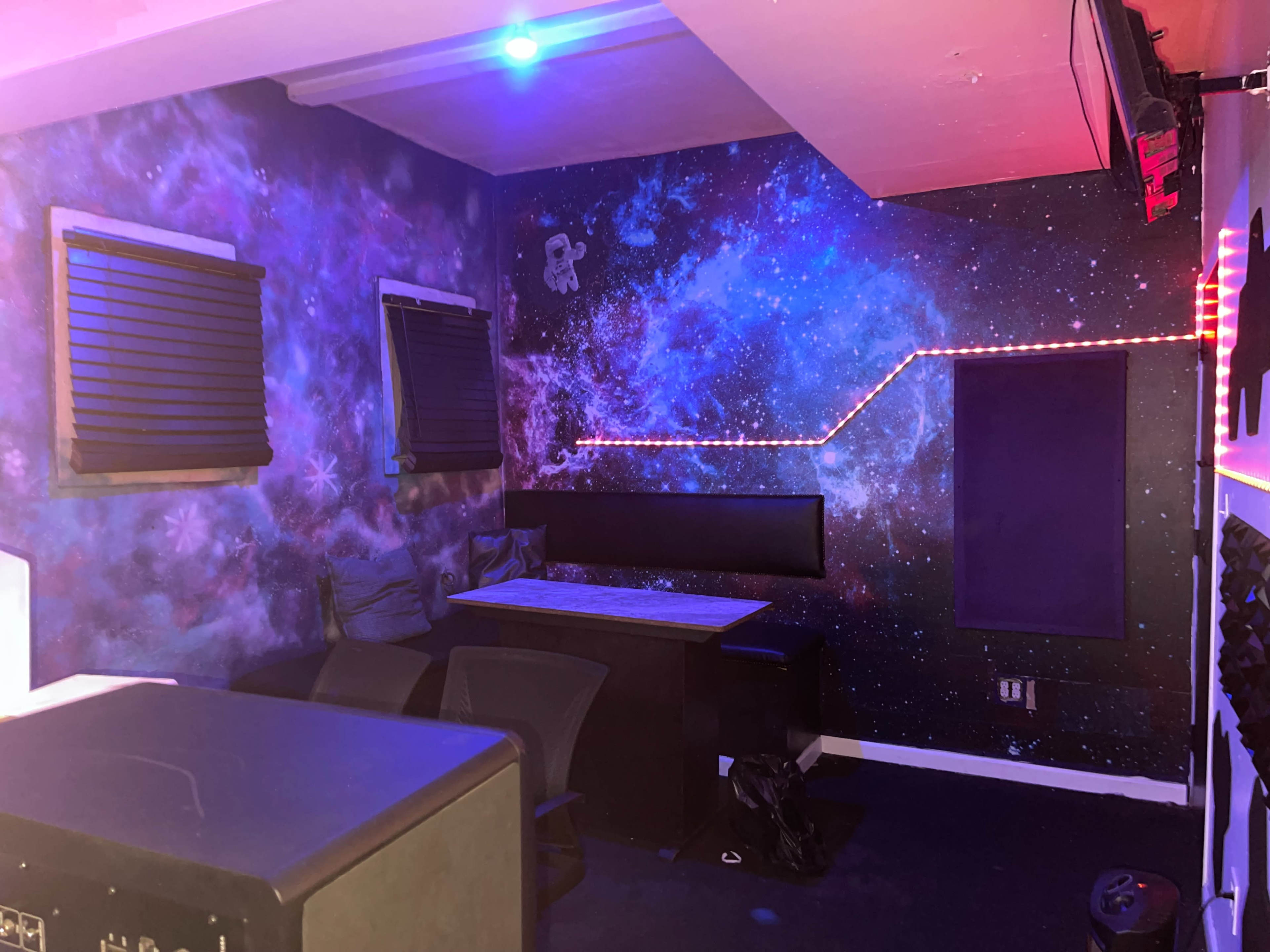 A room with galaxy-themed walls, a table, and chairs positioned against one side.