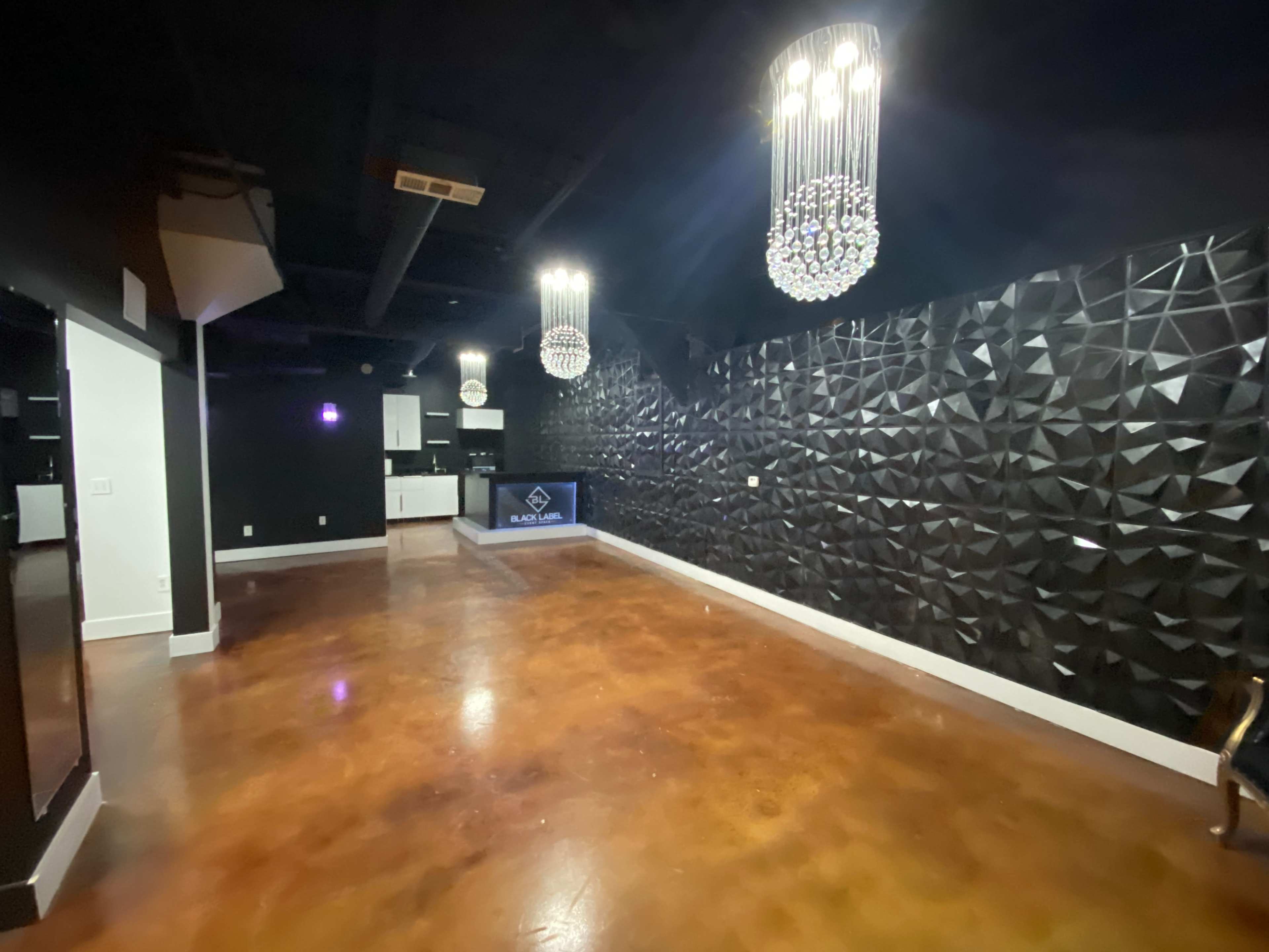 The image shows a modern, empty interior space with textured black walls, pendant chandeliers, and polished concrete flooring.