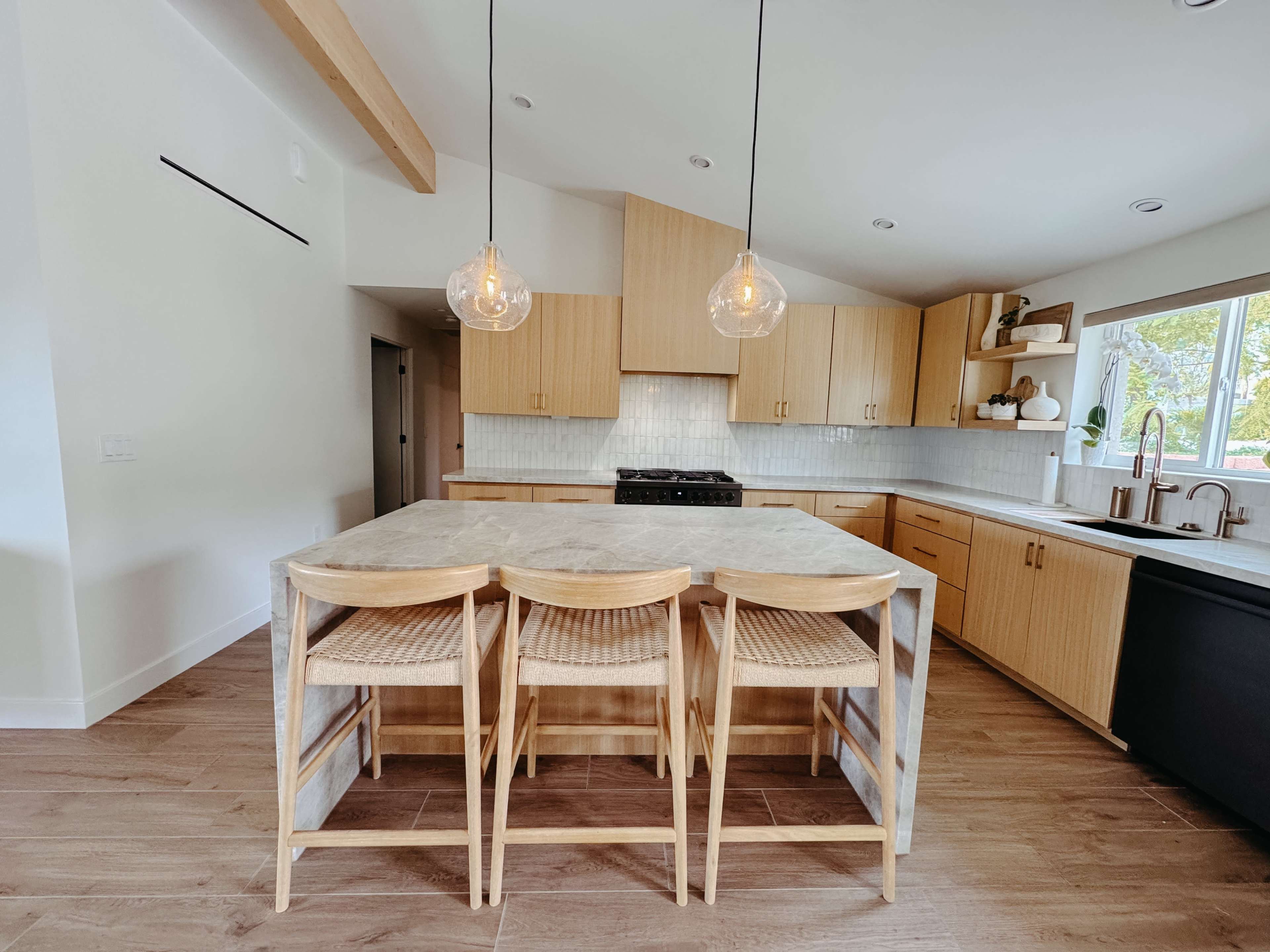 A modern kitchen features light wood cabinetry, a large island with bar stools, and pendant lighting hanging above.