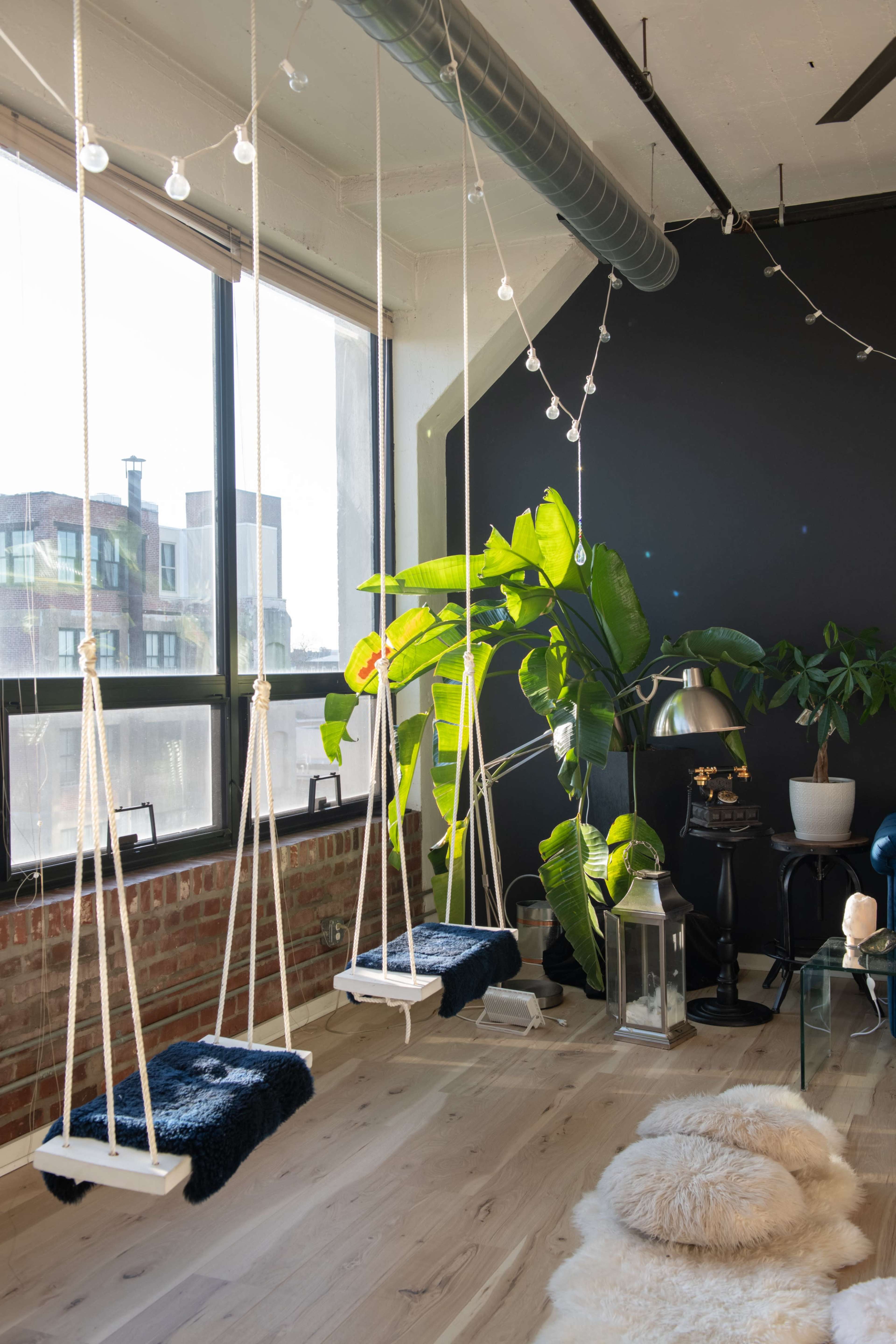 A cozy room features hanging swings near large windows, with a potted plant and a lamp adding to the inviting atmosphere.