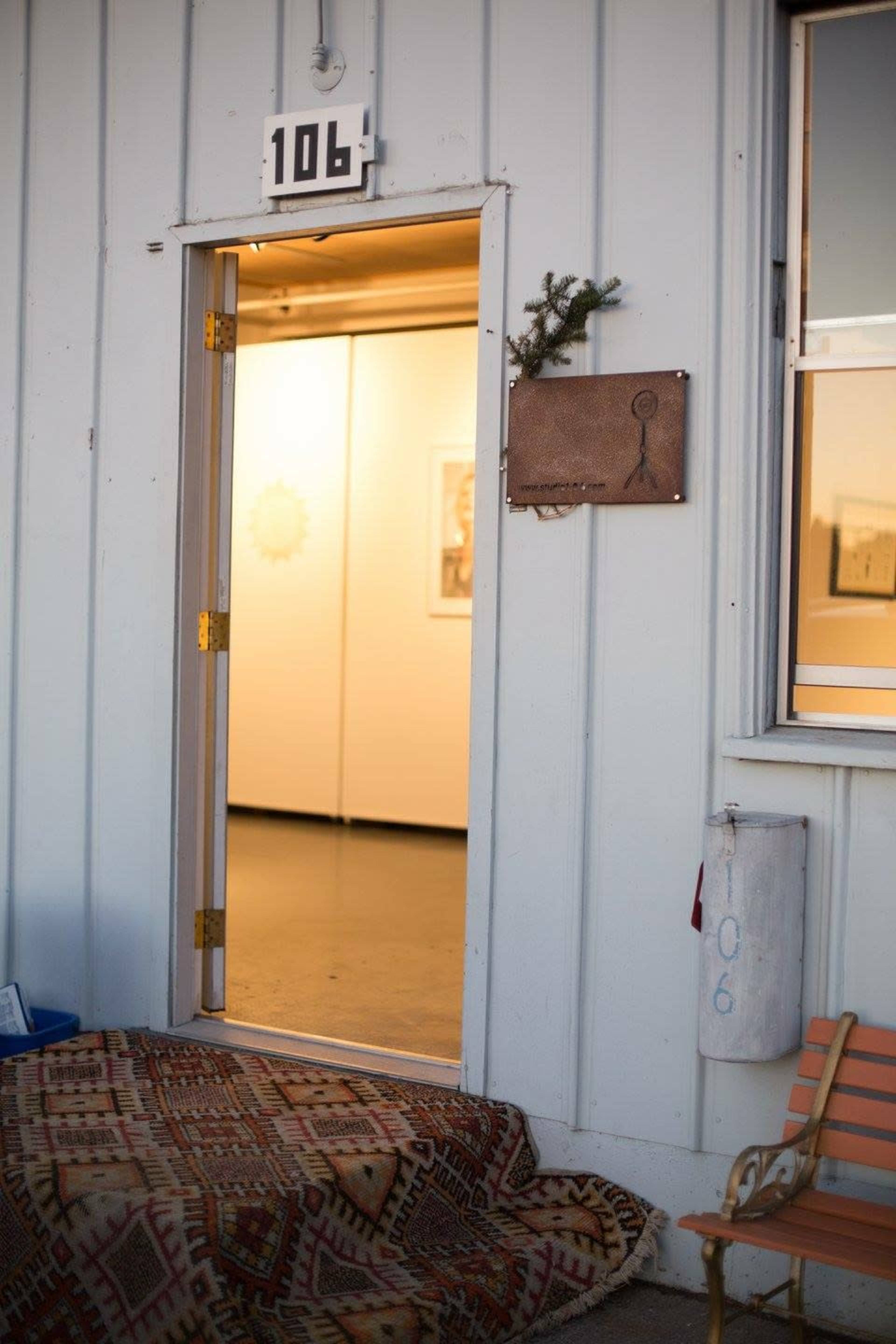 A door marked "106" stands open, revealing a brightly lit interior, with a patterned rug rolled out at its entrance.