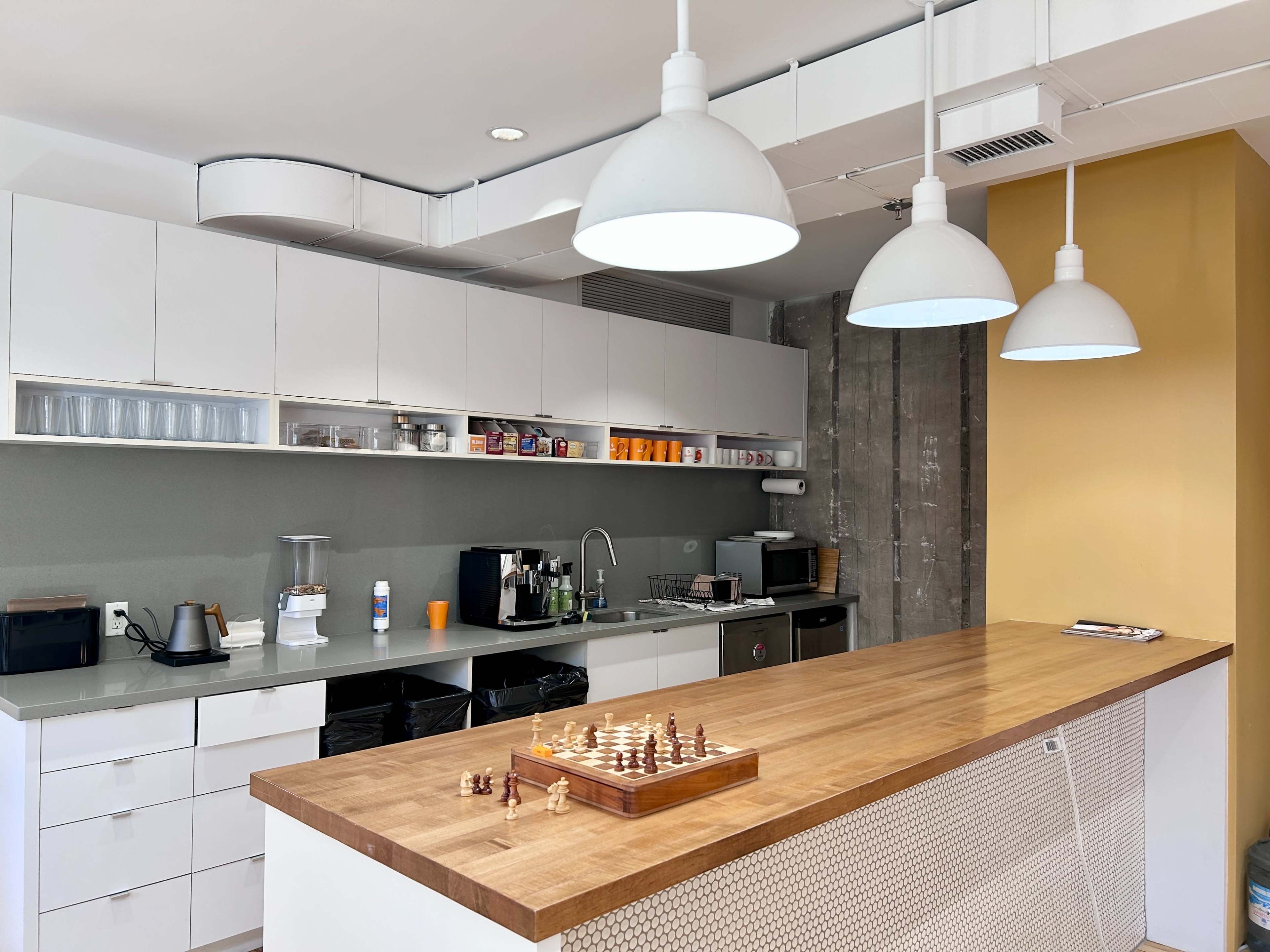 The image shows a modern kitchen with a wooden island, white cabinetry, and three pendant lights hanging above, featuring a chess set on the countertop.
