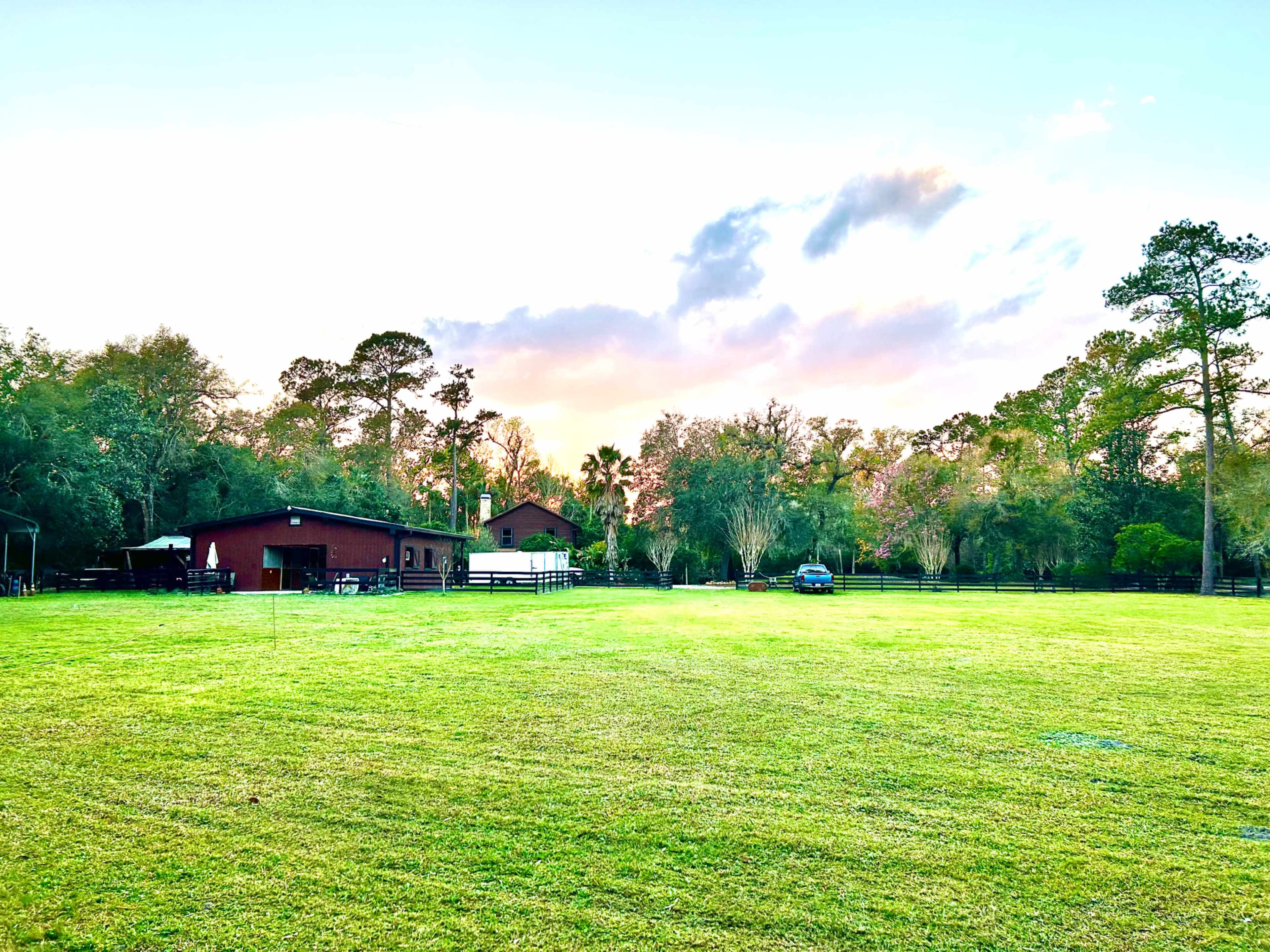A large grassy area features a red barn and a white structure, surrounded by trees and a blue sky with scattered clouds.