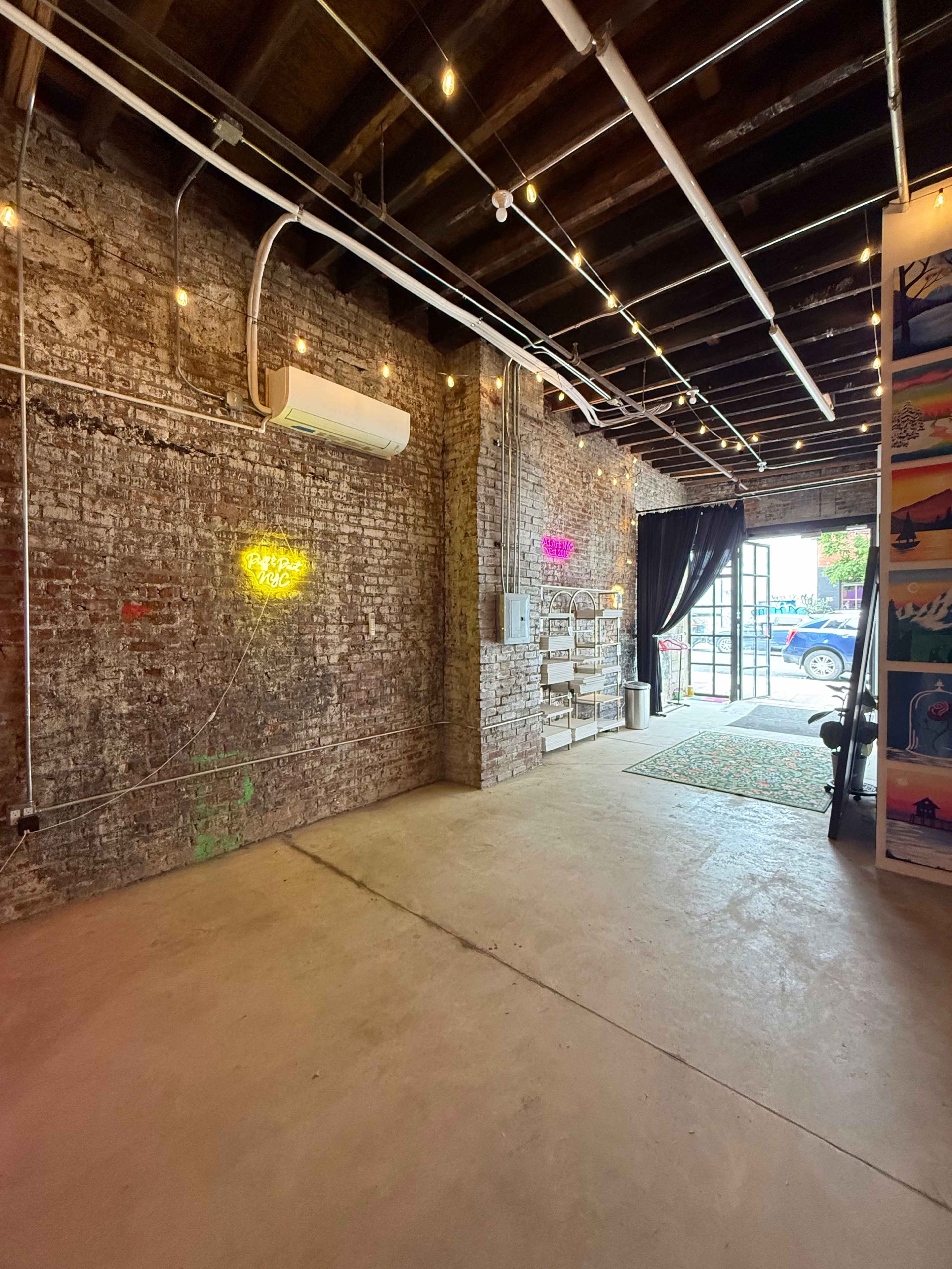 The image shows an empty interior space with exposed brick walls, overhead lighting, and an open doorway leading to the outside.