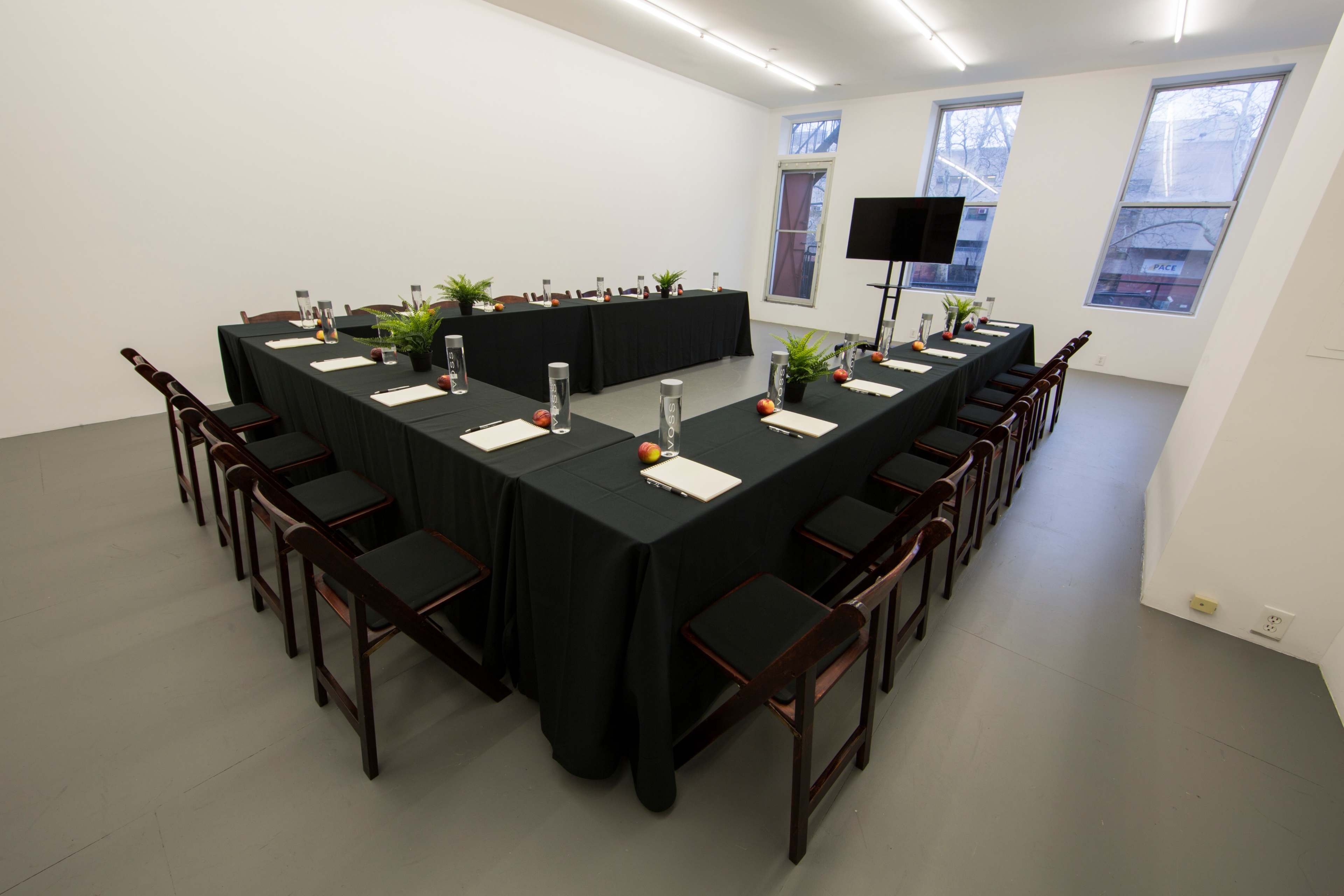 A rectangular conference table is set up in a minimalist room with chairs around it, featuring drinks and stationery on the surfaces.
