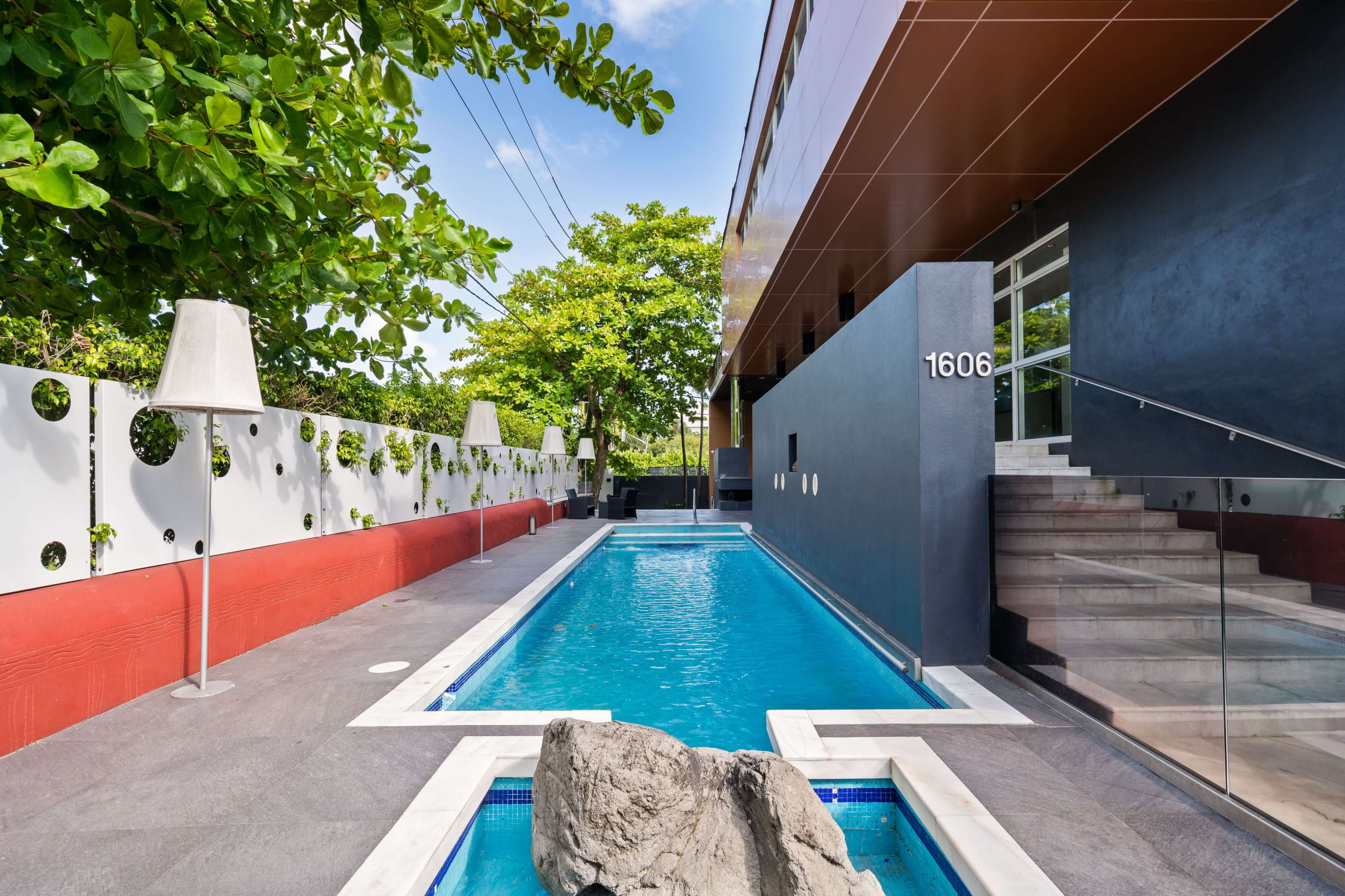 A modern building with a long, narrow swimming pool bordered by sleek landscaping and steps leading to an entrance.