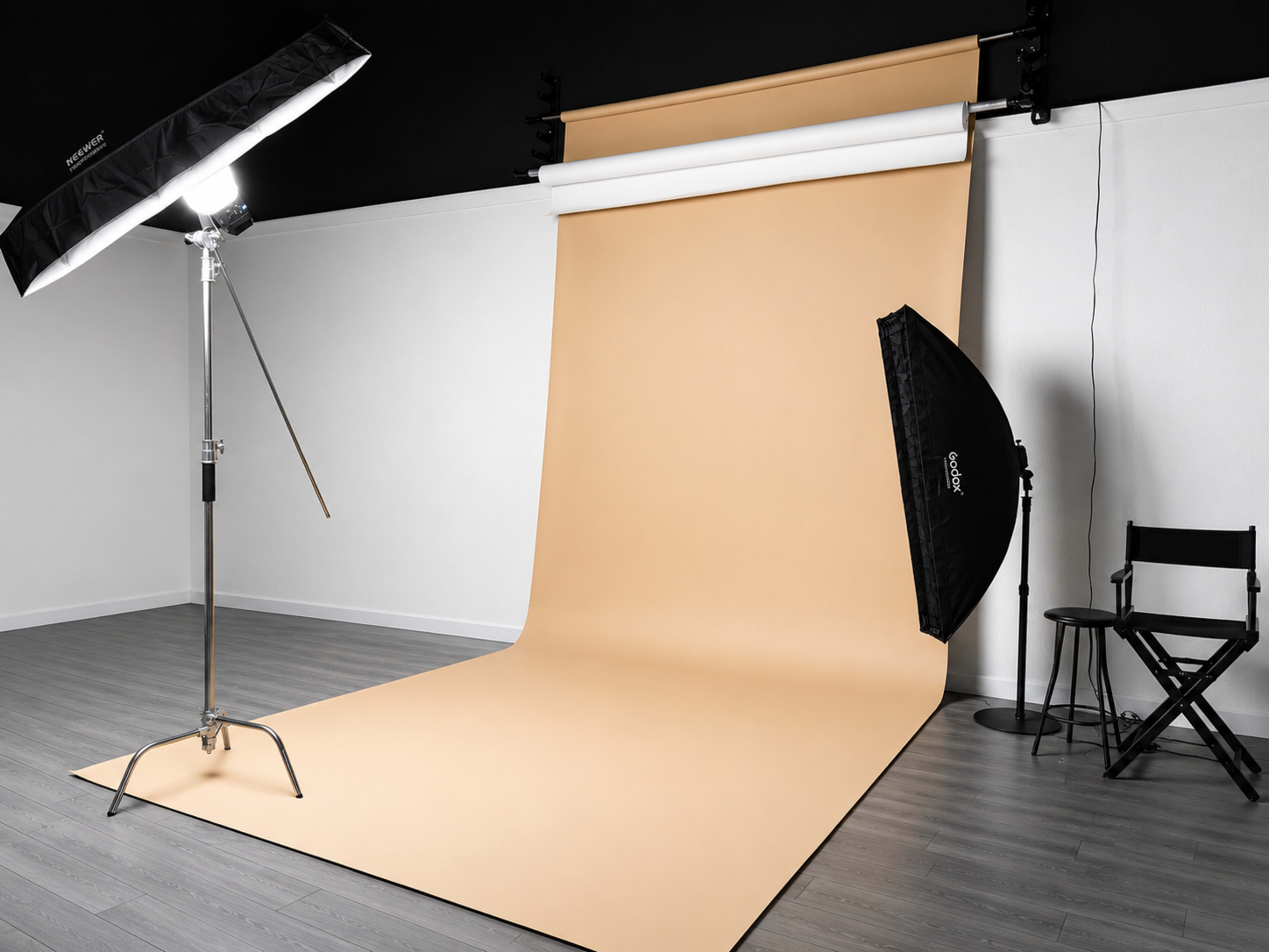 The image shows a photography studio equipped with a light source, a large beige backdrop, and a simple black director's chair against a white wall.