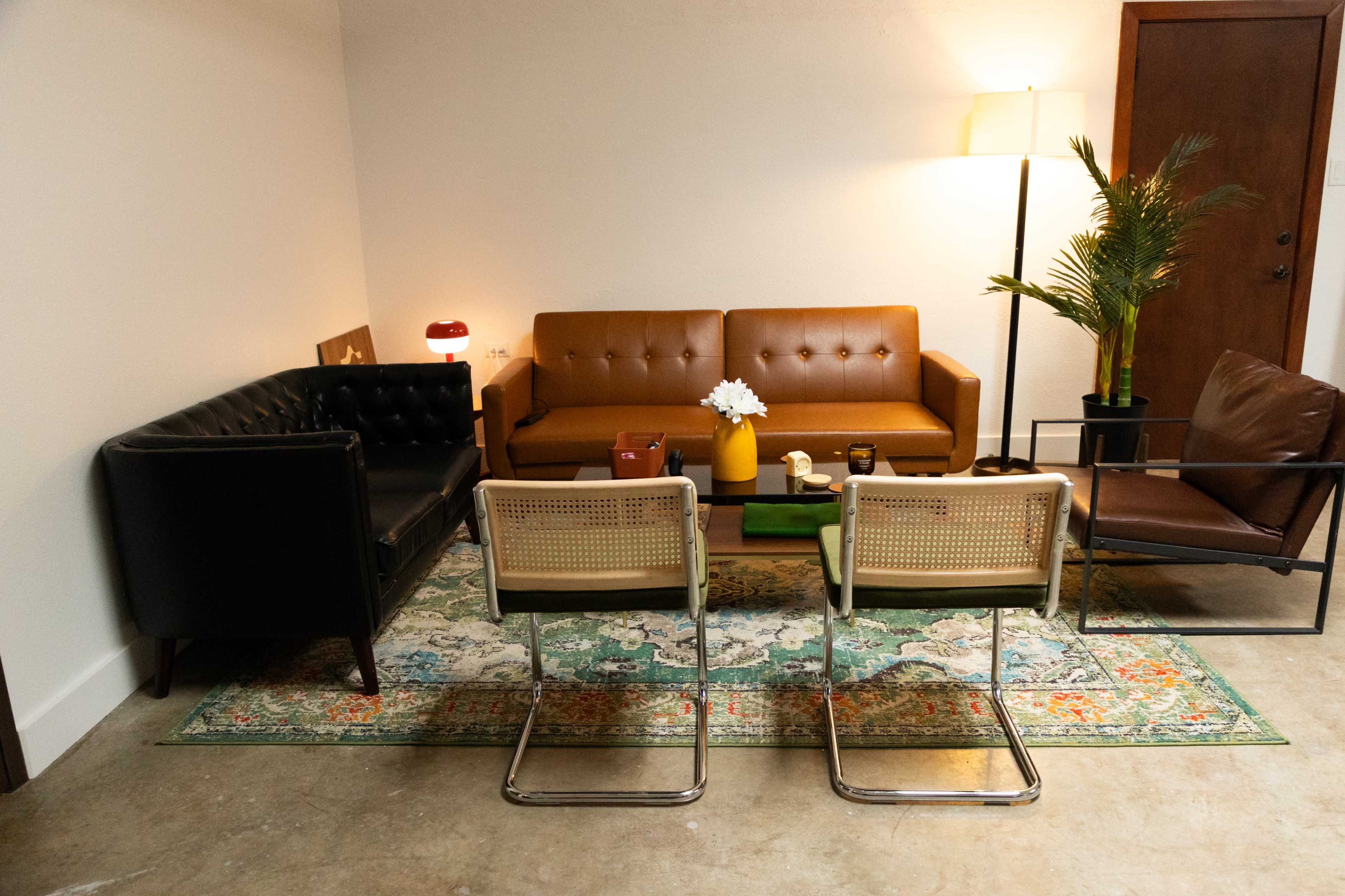 The image shows a cozy living room with a mix of leather and upholstered furniture arranged around a decorative rug.