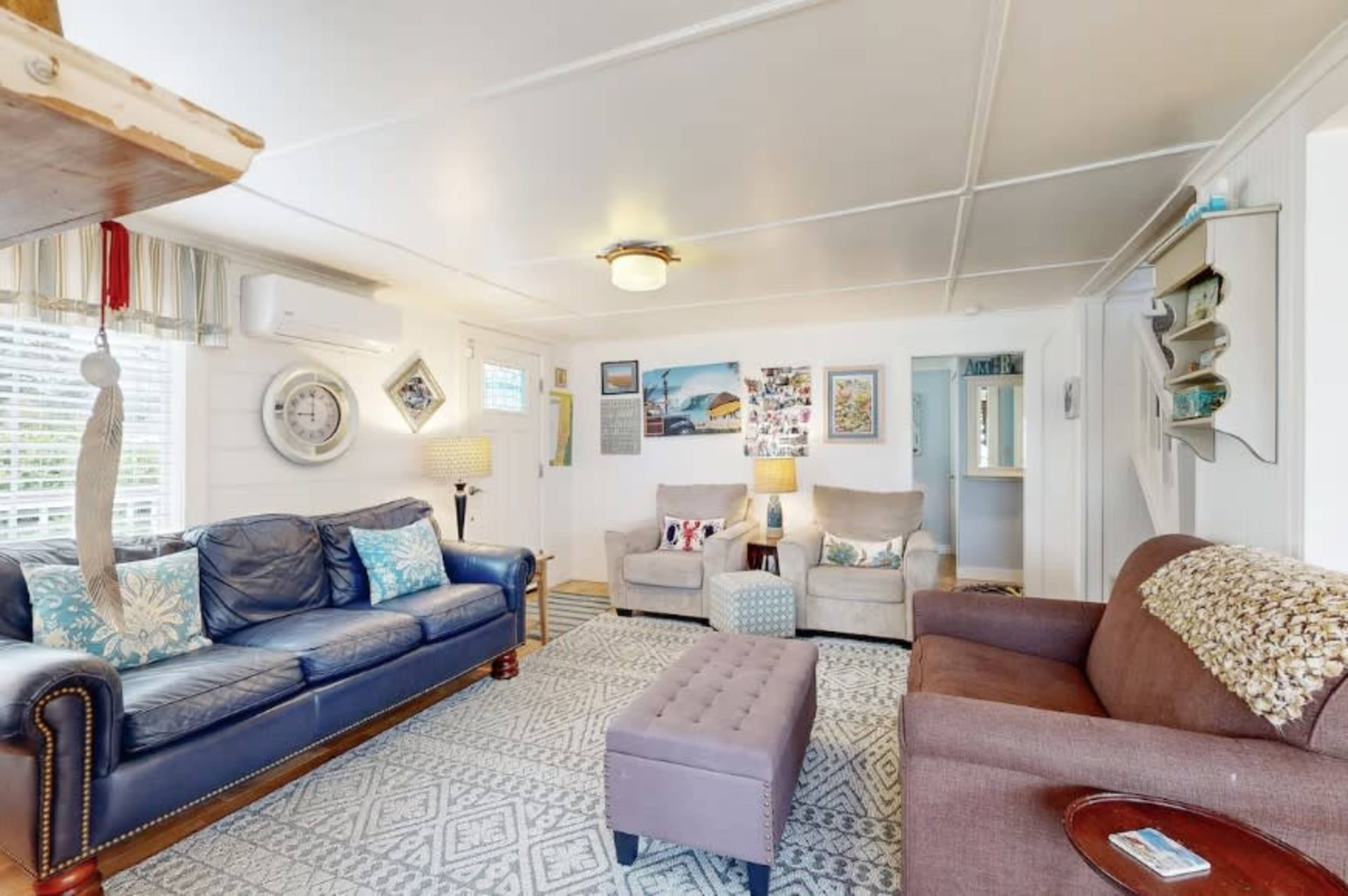 The image shows a cozy living room featuring a blue leather sofa, two beige armchairs, and a gray ottoman on a patterned rug.